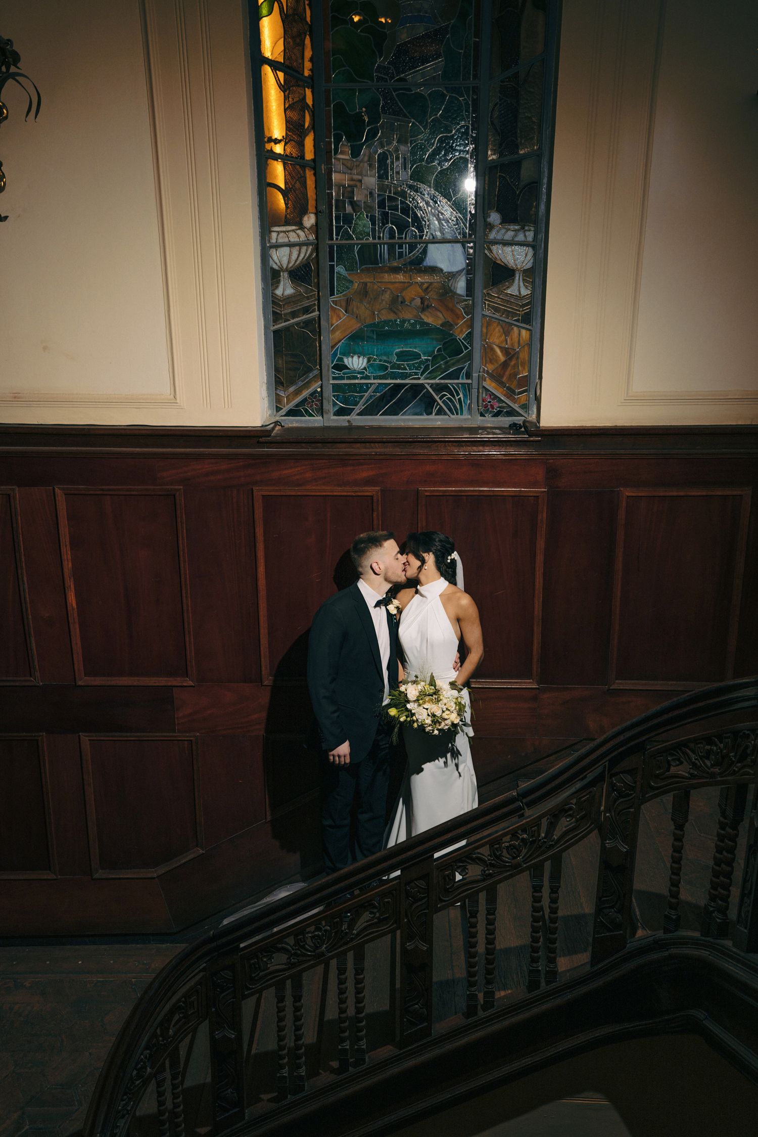 Romantic couple portrait on dark wooden staircase with stained glass windows.