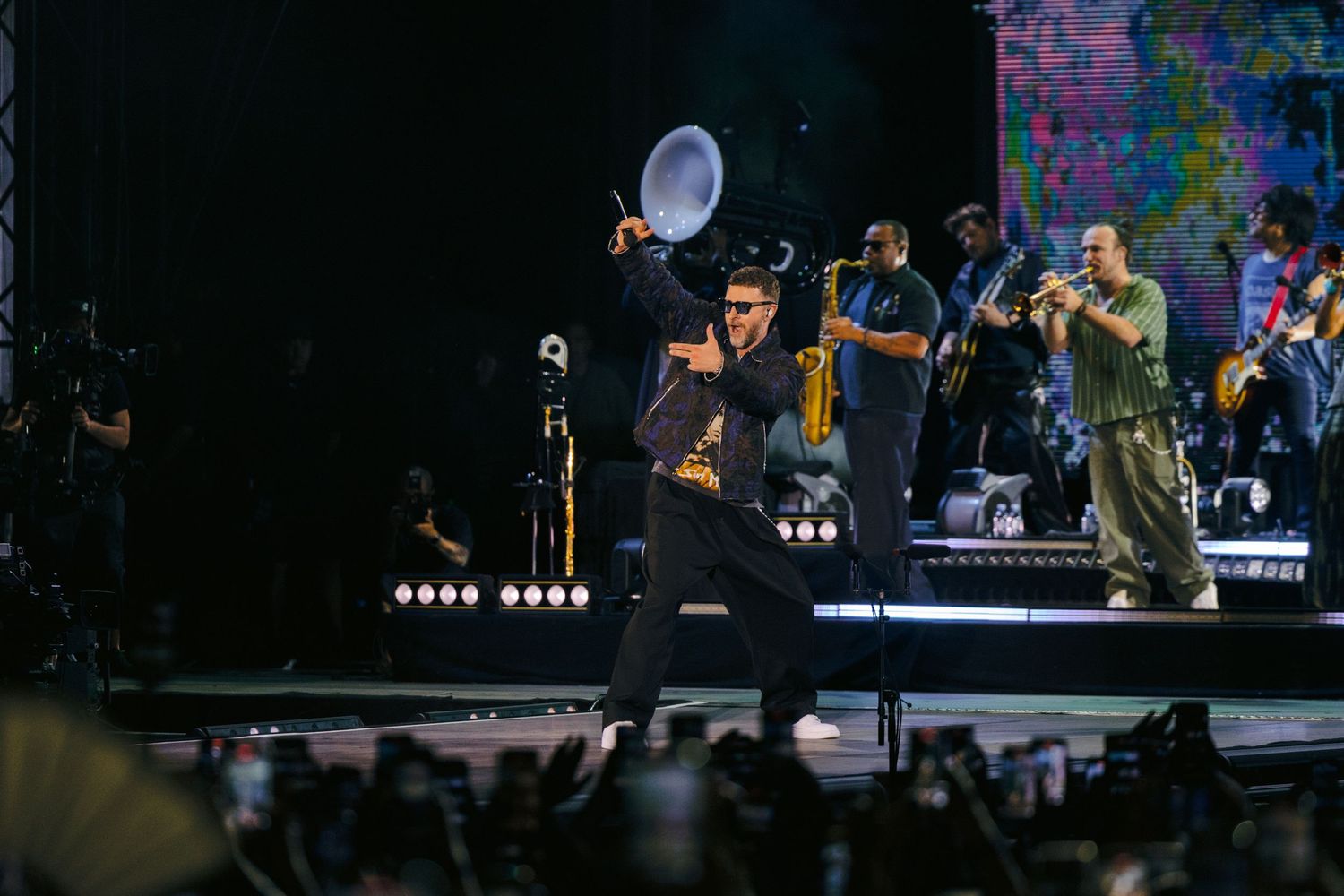 Band members perform energetically on illuminated stage during nighttime concert.