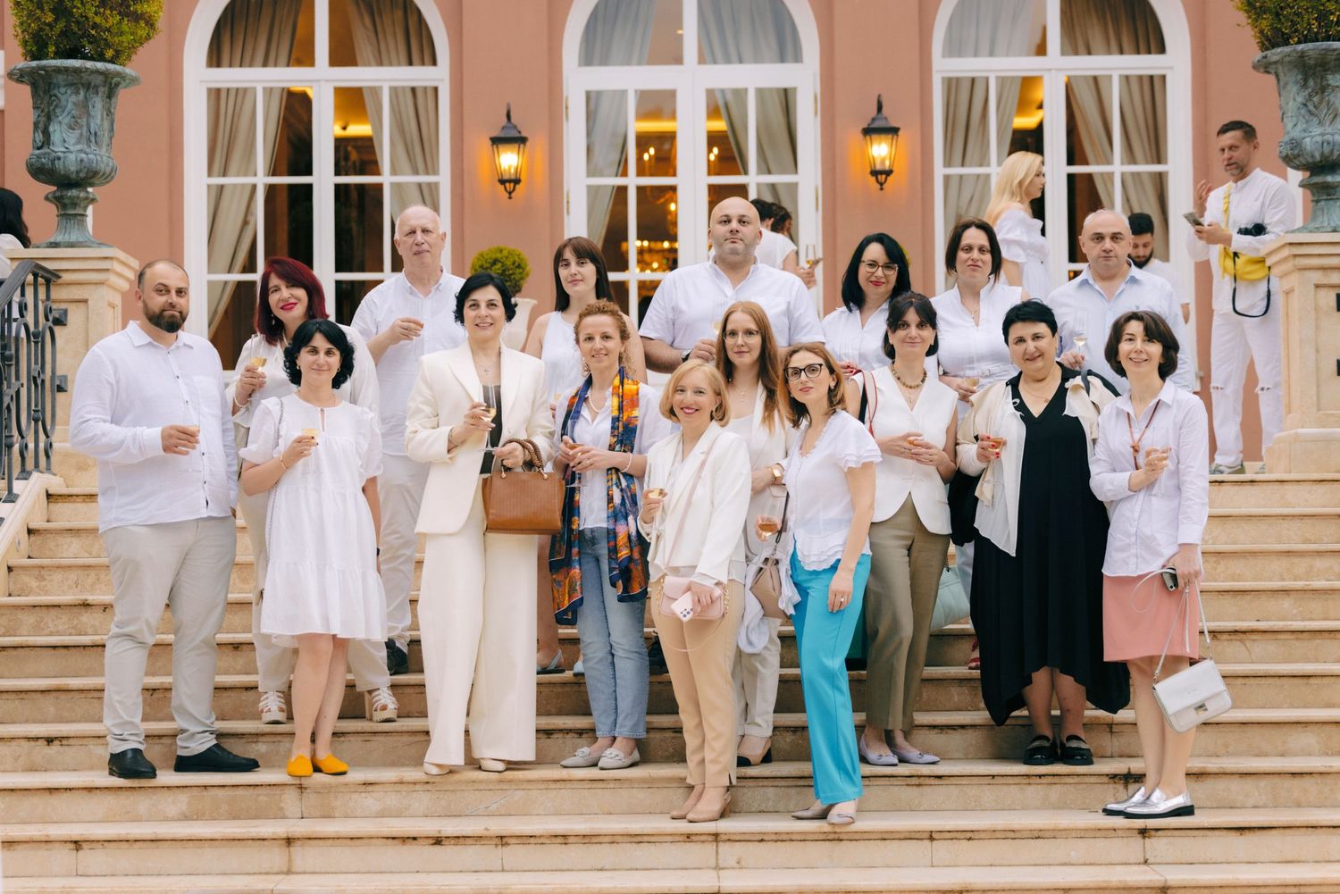 Large group photo of guests in white attire on grand building steps.