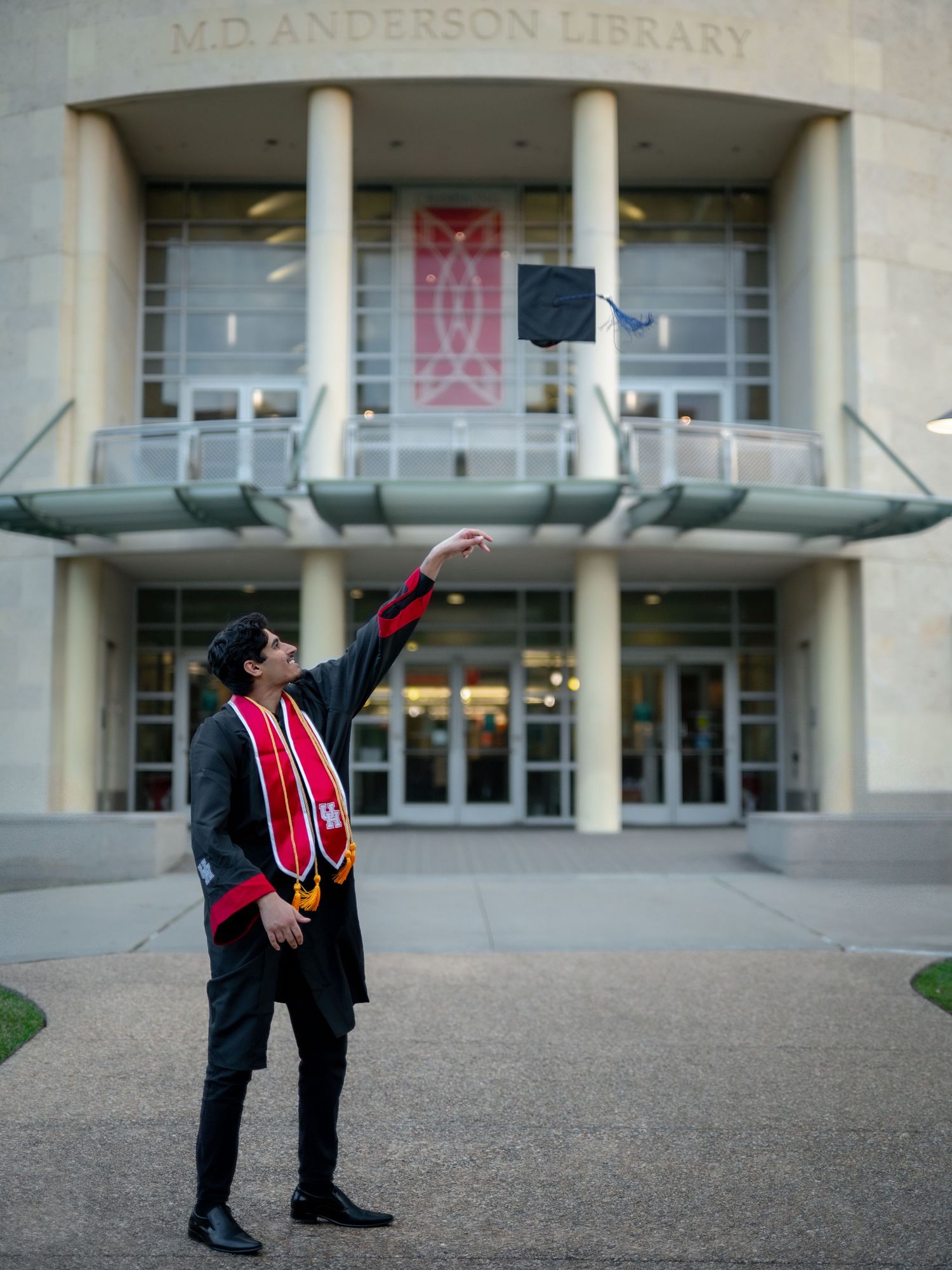 Graduate poses energetically outside MD Anderson Library in full graduation attire.