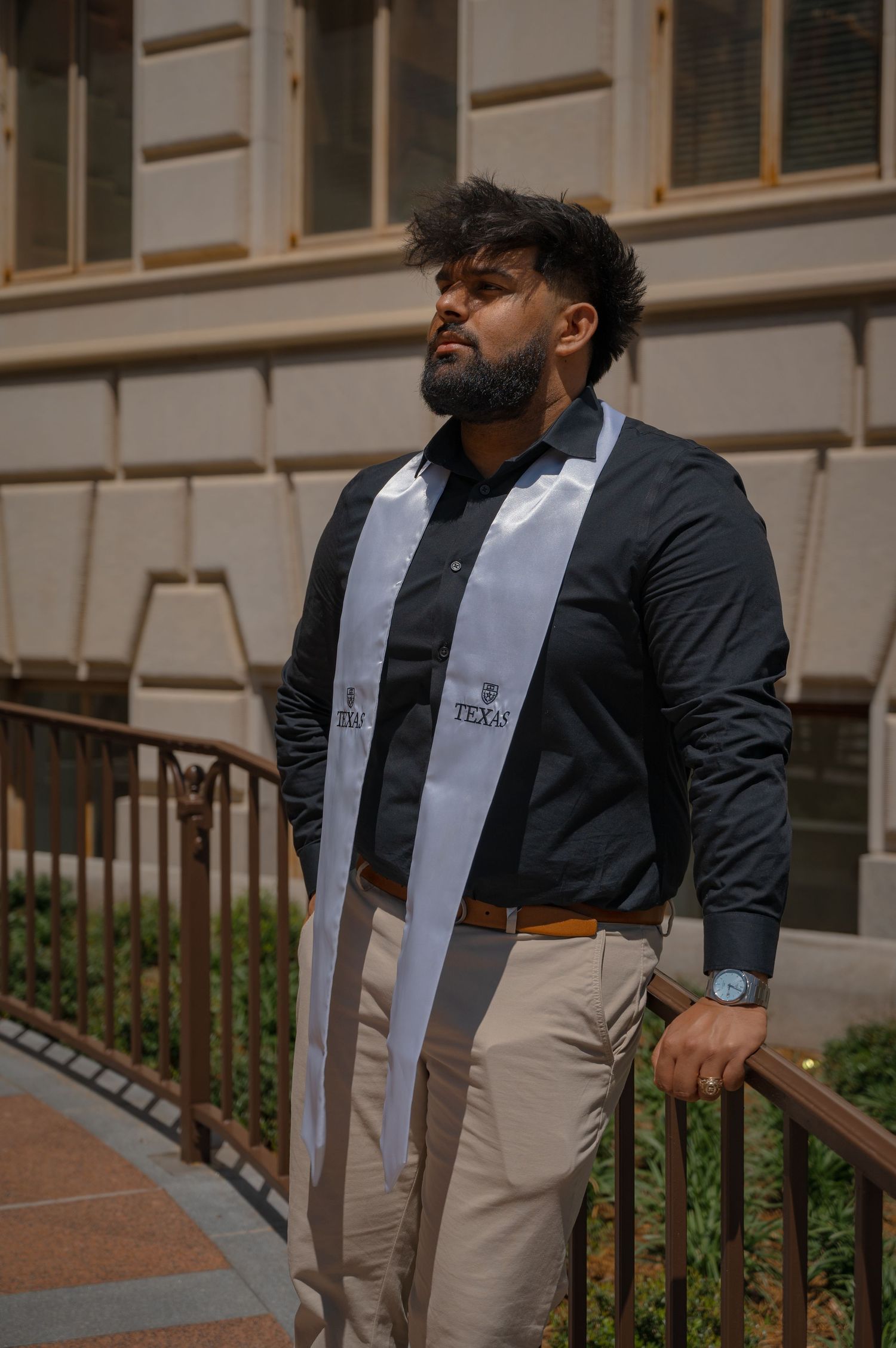 Graduate wearing Texas stole poses near railing on campus steps.