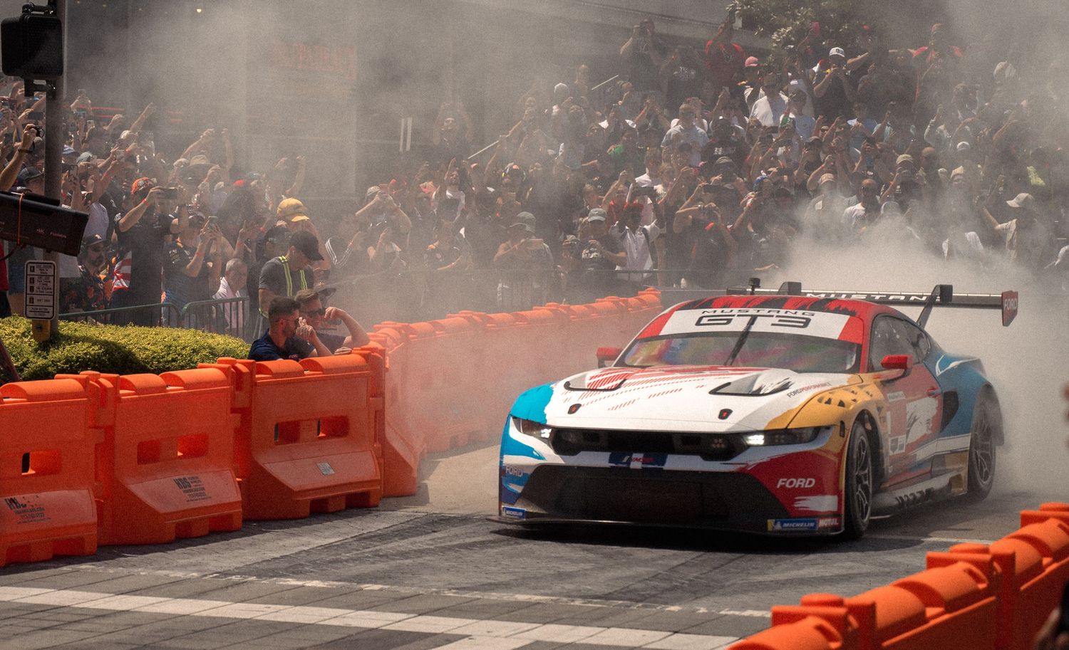 Formula 1 car kicks up tire smoke while performing donuts during a street demonstration event.