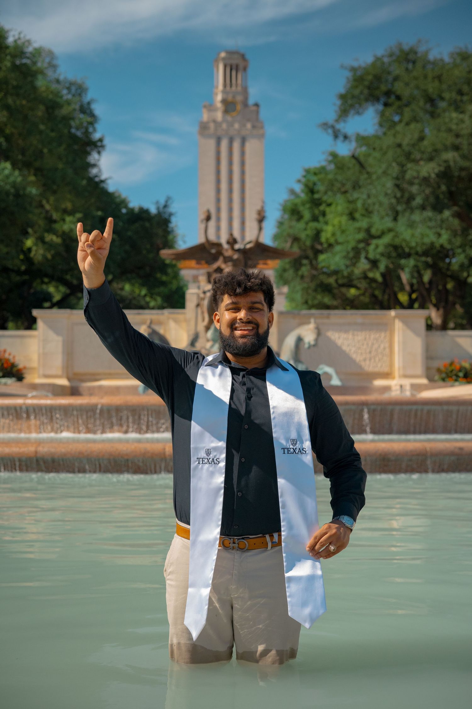 Graduate celebrates in fountain with UT Austin Tower visible in background.
