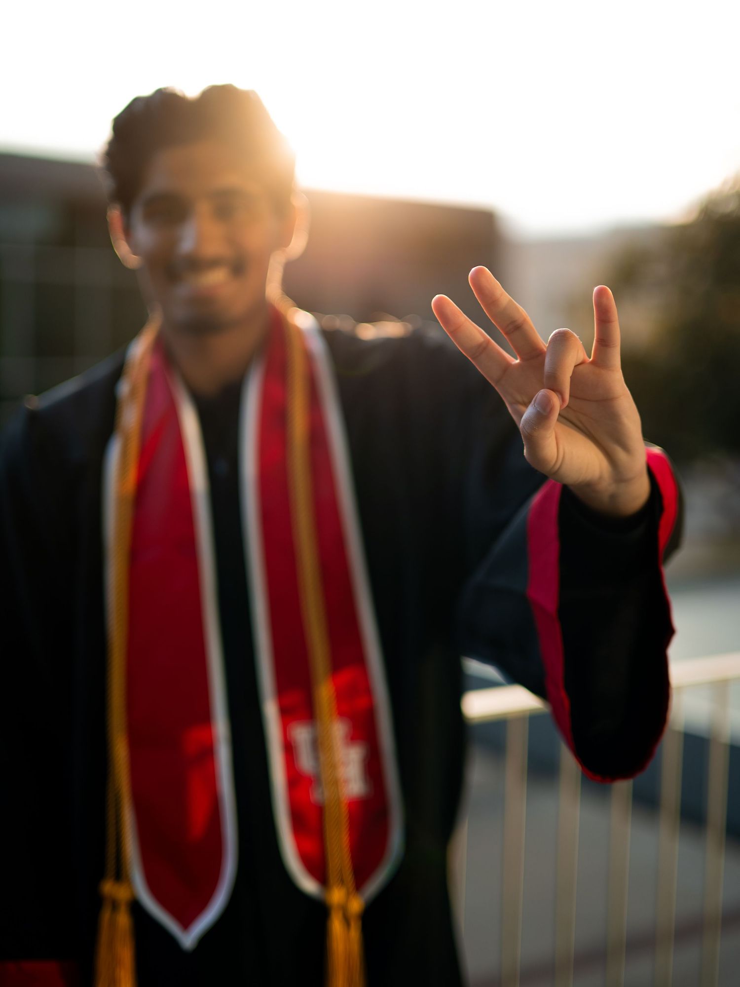 Graduate in academic regalia gestures expressively during sunset photo session.
