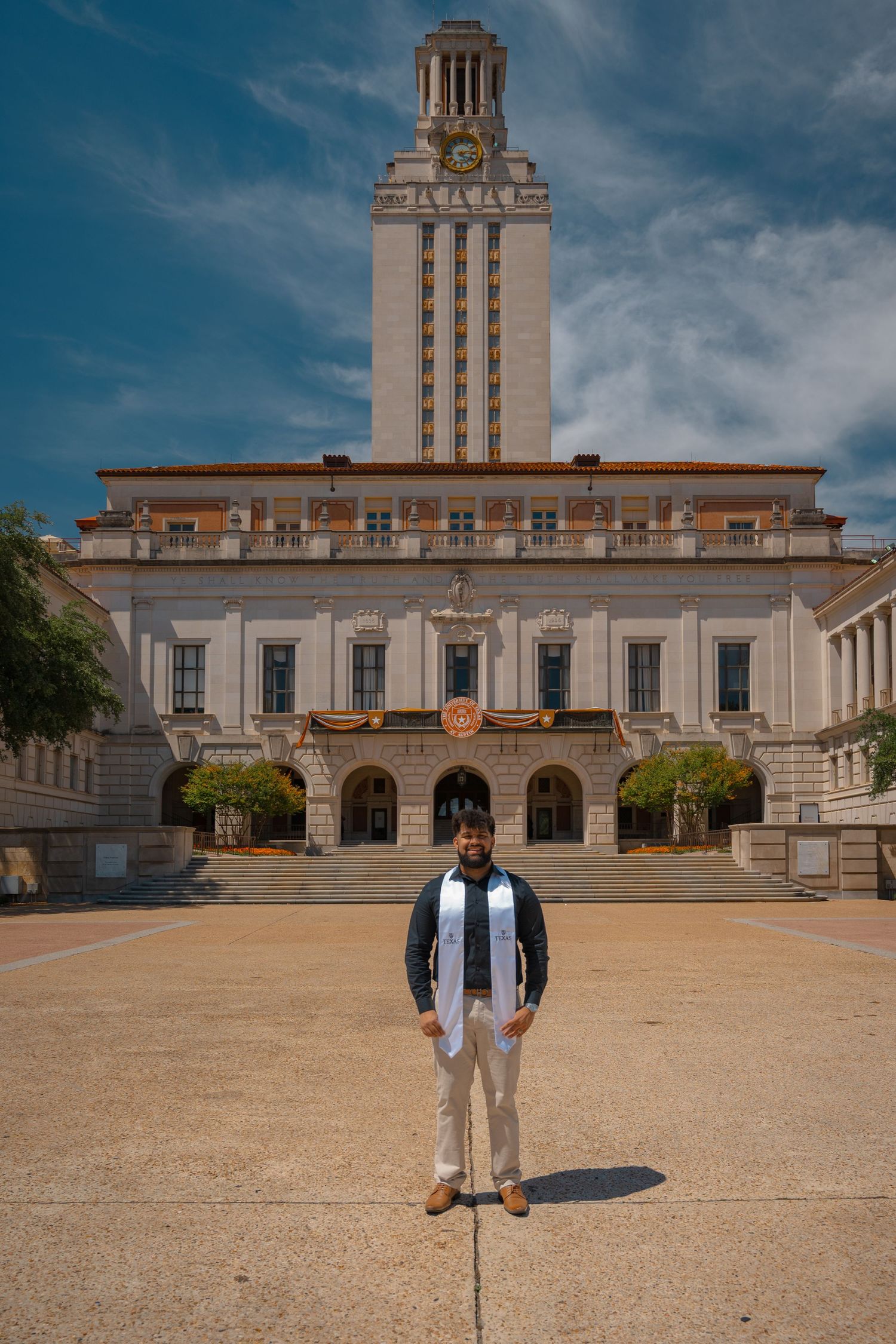 Graduate stands proudly in front of the University of Texas main building on graduation day.