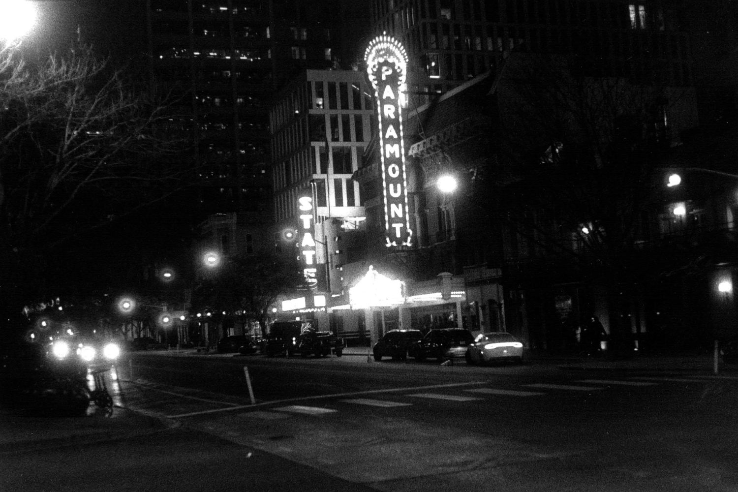 Night view of city street with glowing lights and historic buildings in monochrome.