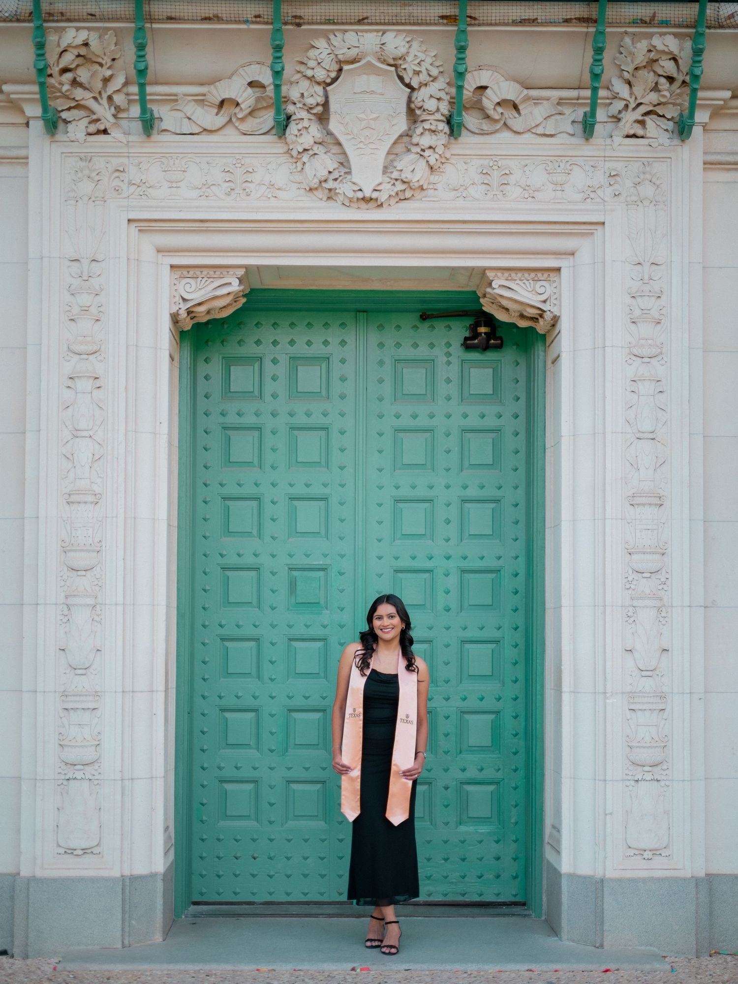 A person stands in front of a grand turquoise door with ornate white architectural details and decorative moldings.