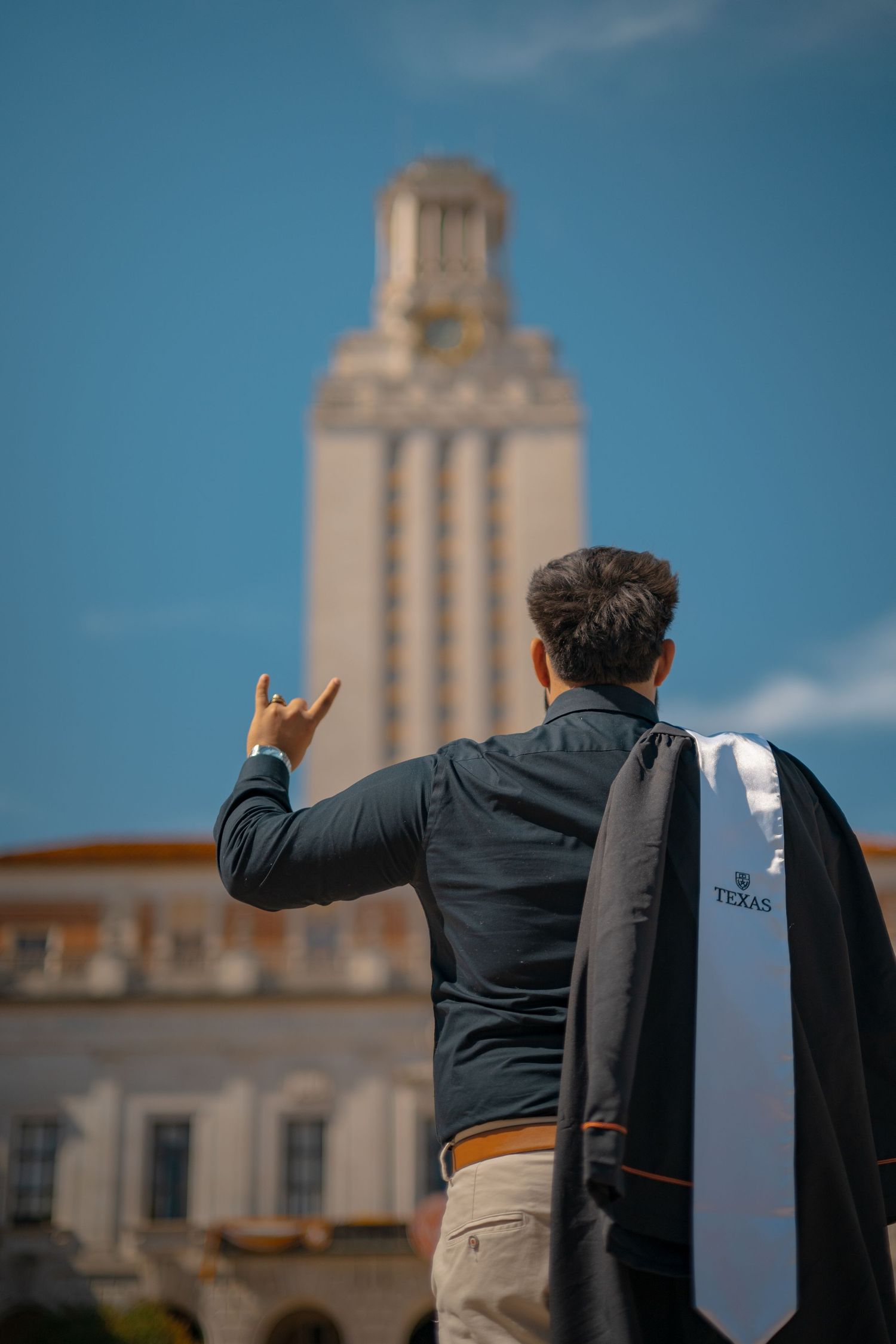 Back view of graduation attire with the UT Tower rising majestically in the background.