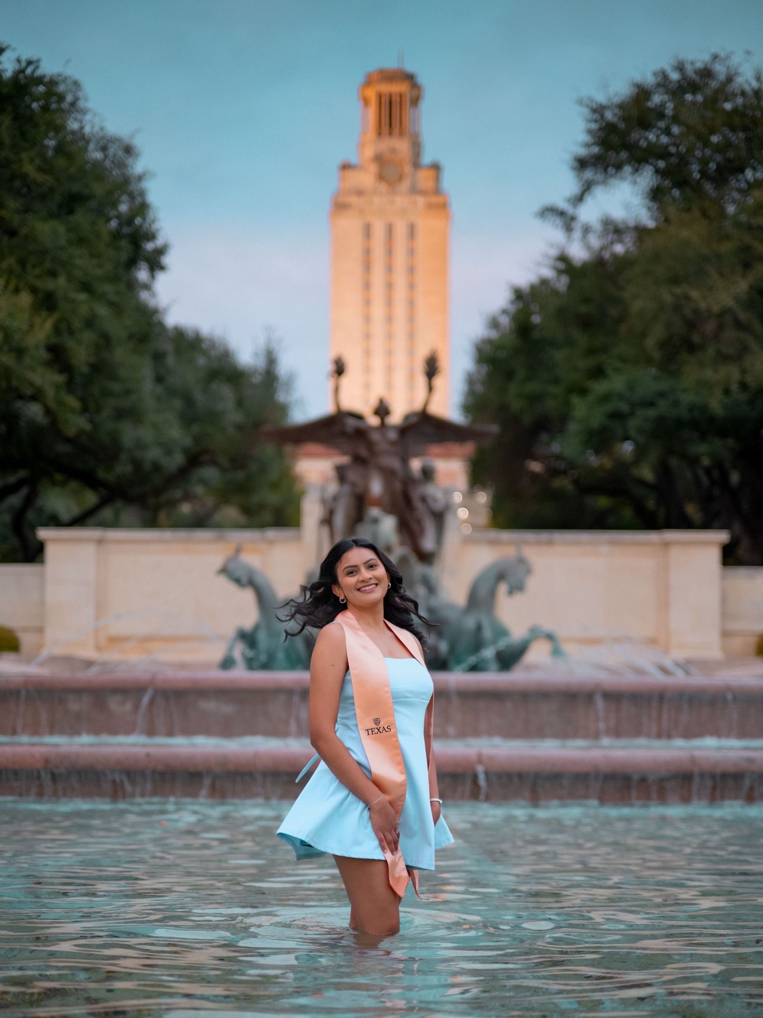 Woman posing in a light blue dress in front of the iconic UT Austin Tower during a photoshoot session.