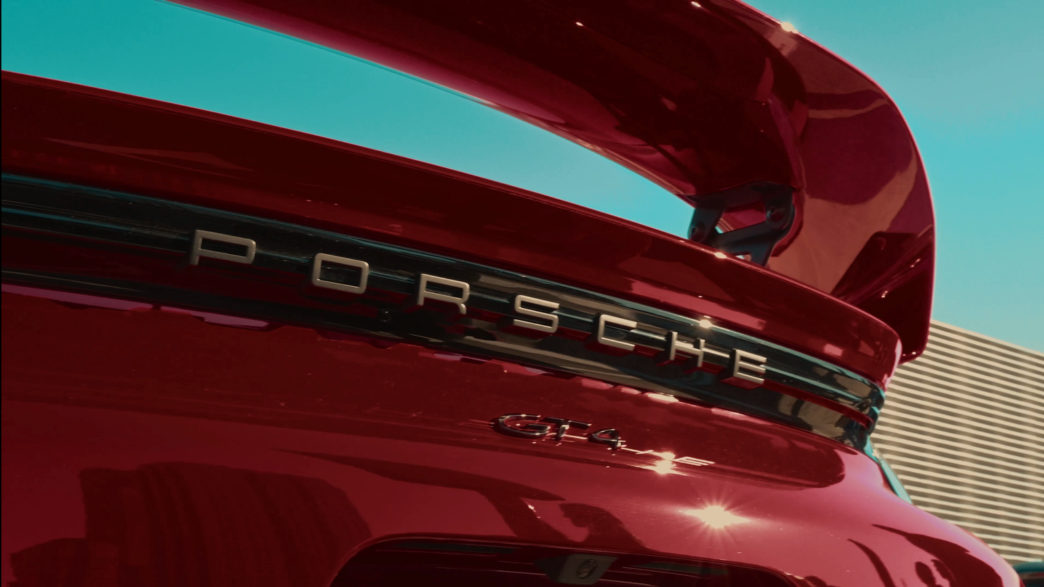 Red Porsche lettering detail on sports car exterior against blue sky.