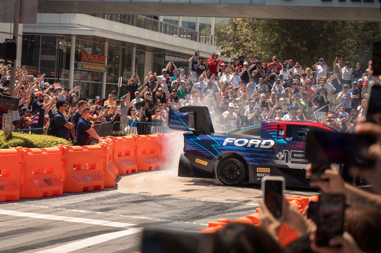 Racing cars navigate tight corners between buildings during an urban motorsport demonstration event.
