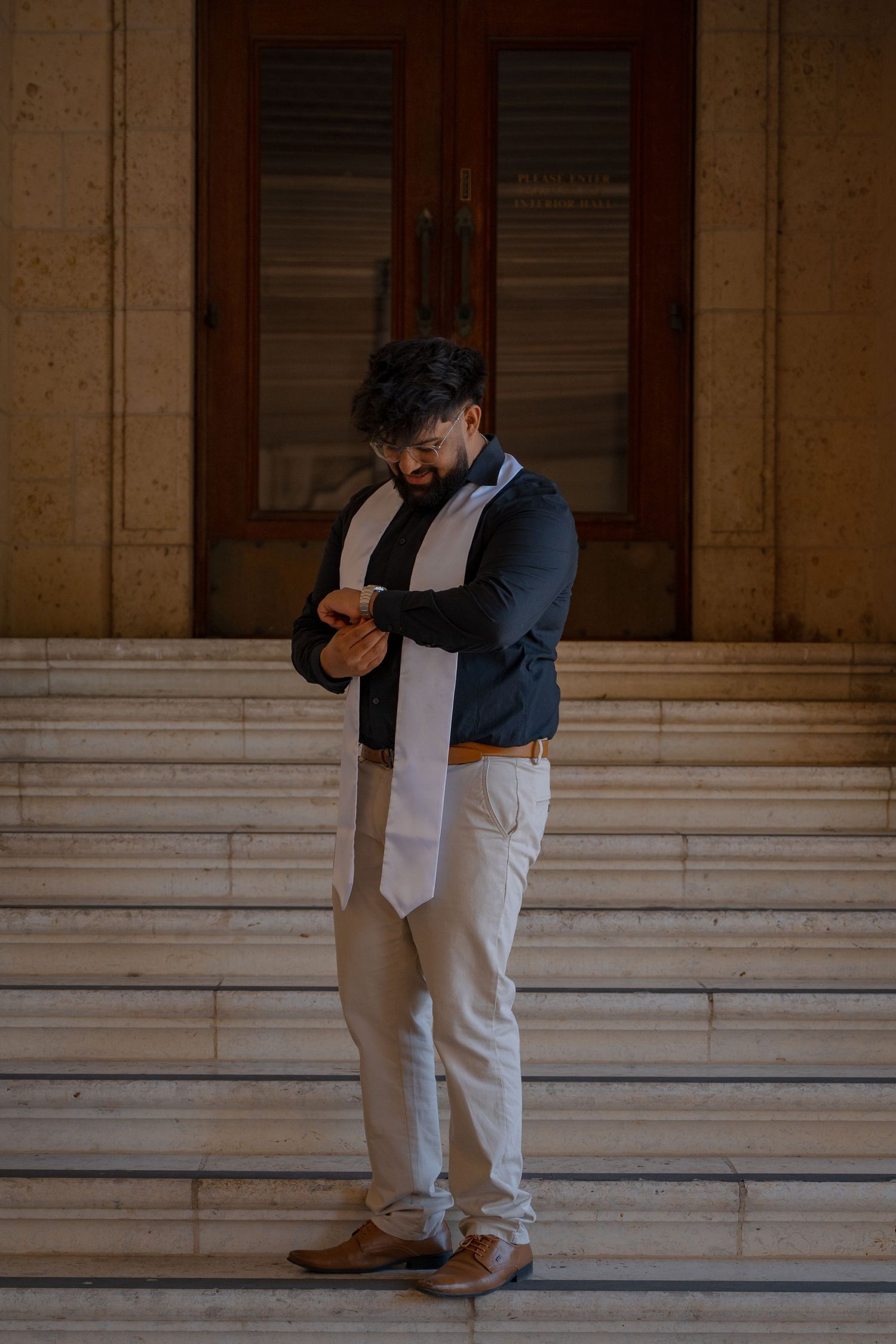 Graduate in formal attire poses thoughtfully inside historic campus building.