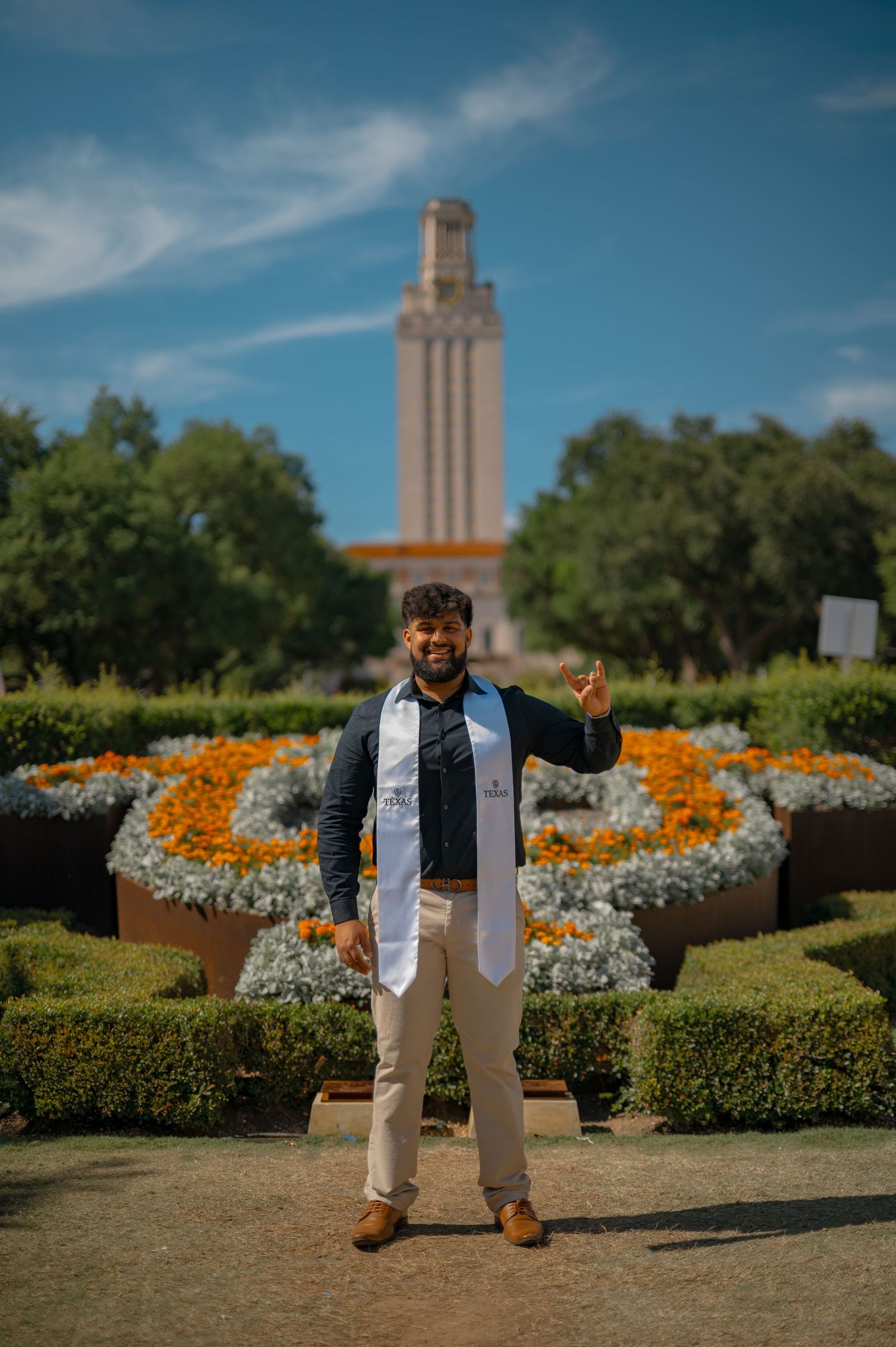 Graduate celebrates in front of UT Tower with decorative floral arrangement in foreground.