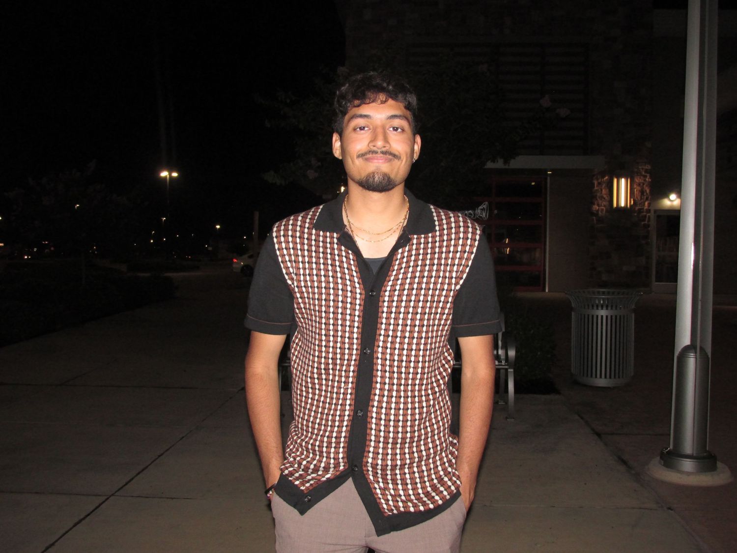 Person wearing checkered vest standing outside at night.