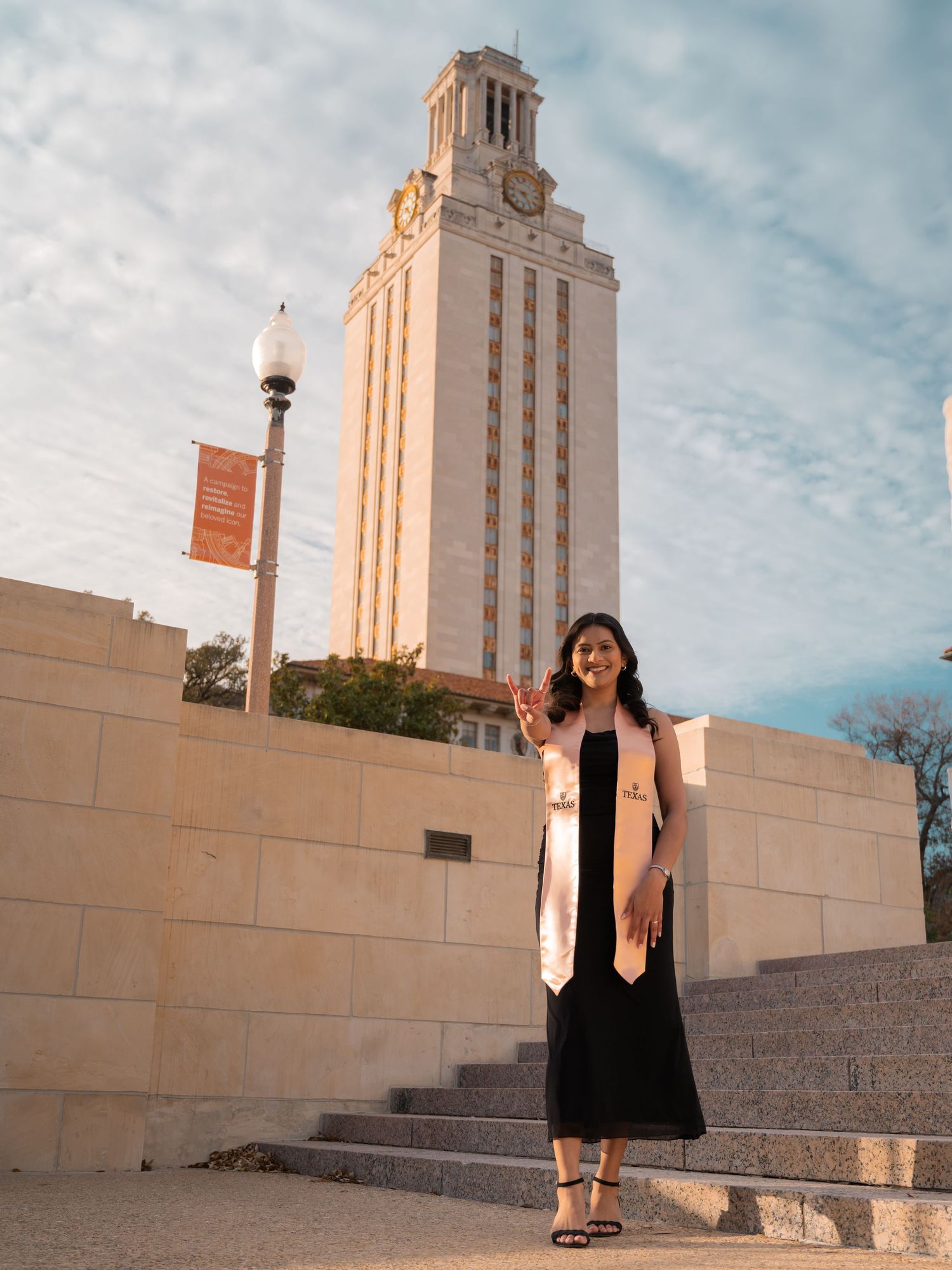 A graduate poses in front of the iconic University of Texas Tower in Austin during golden hour.