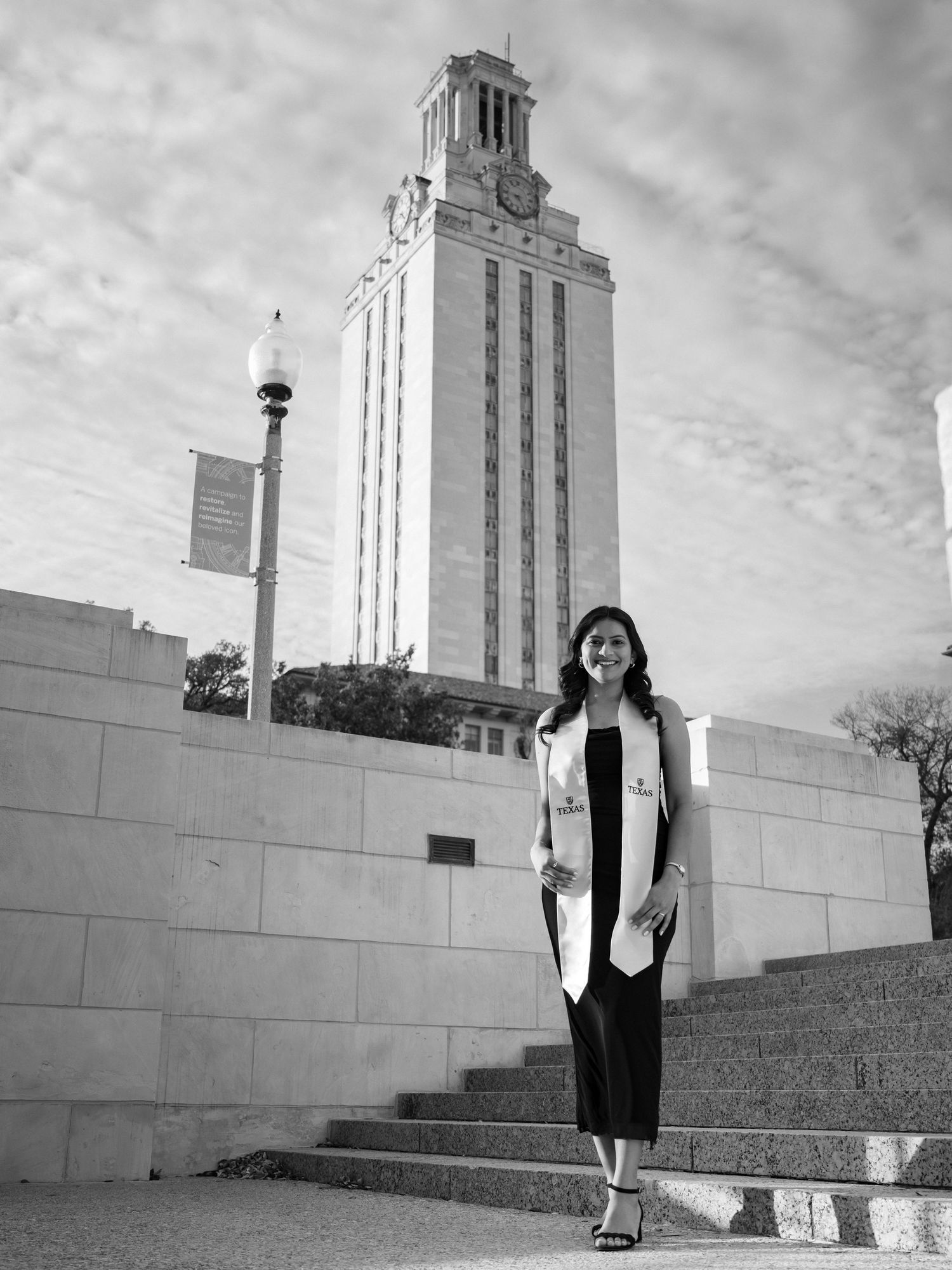Black and white photo of someone standing on steps in front of the University of Texas Tower on a cloudy day.