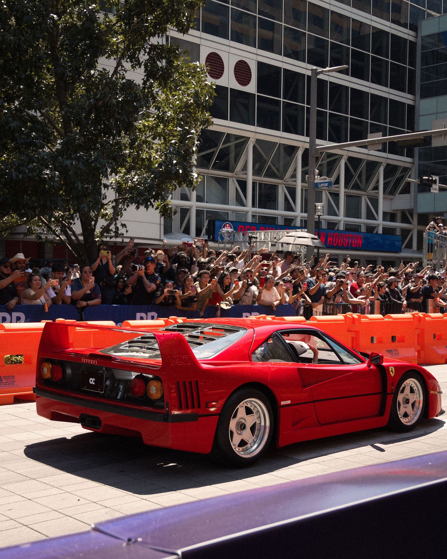 Red Ferrari sports car driving on demonstration course with orange safety barriers.