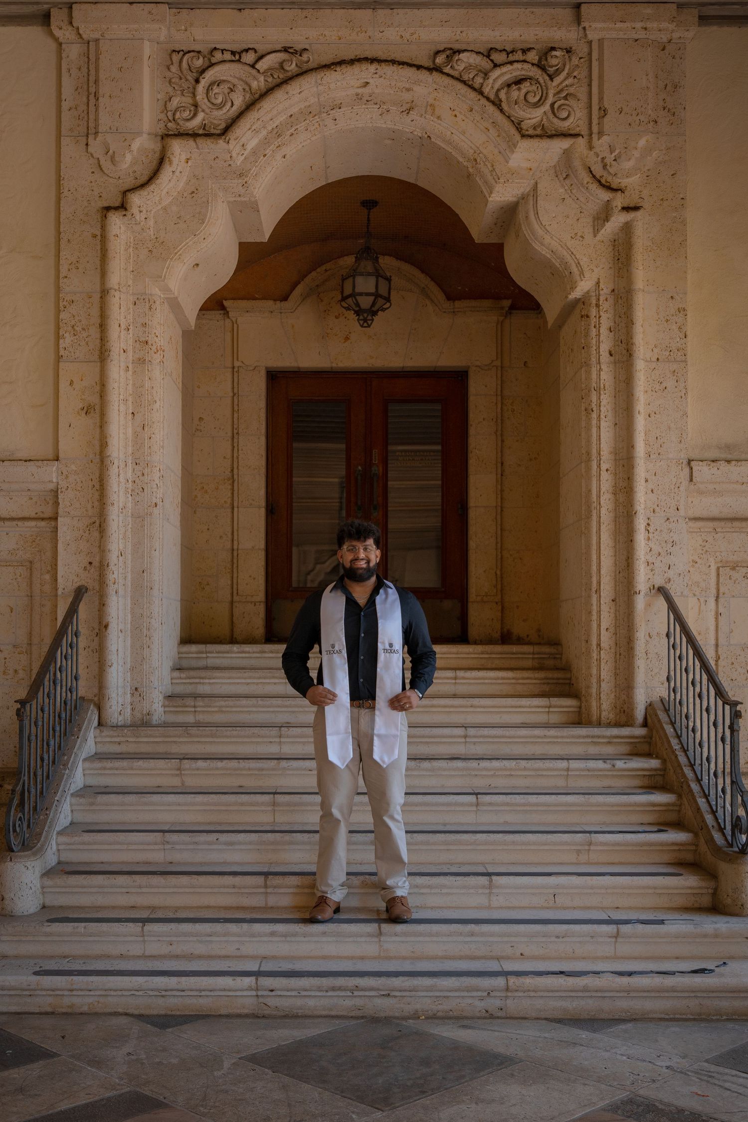 Graduate stands in ornate stone archway of historic university building.
