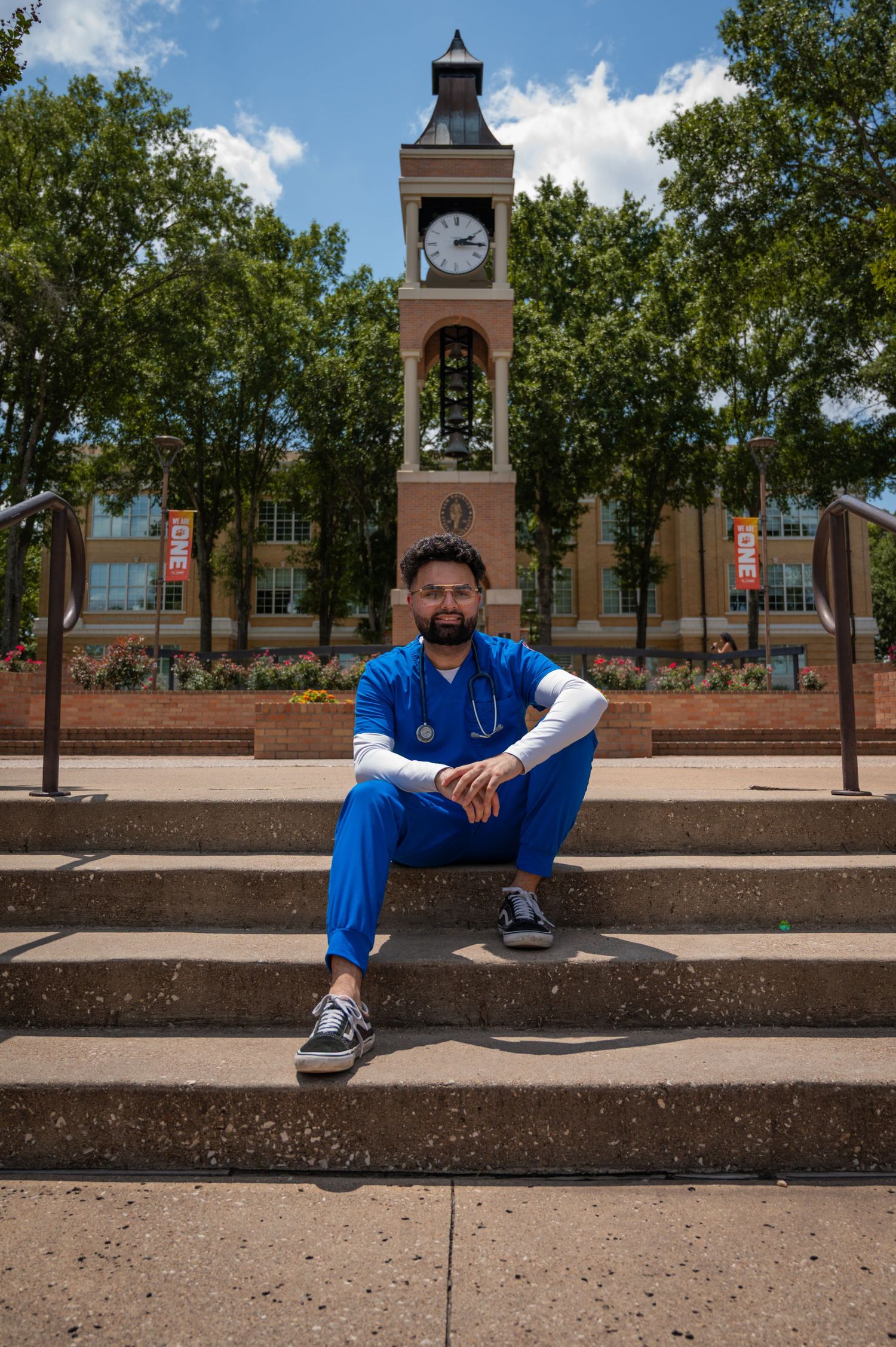 Student in blue attire sitting on a brick ledge with campus clock tower in background.