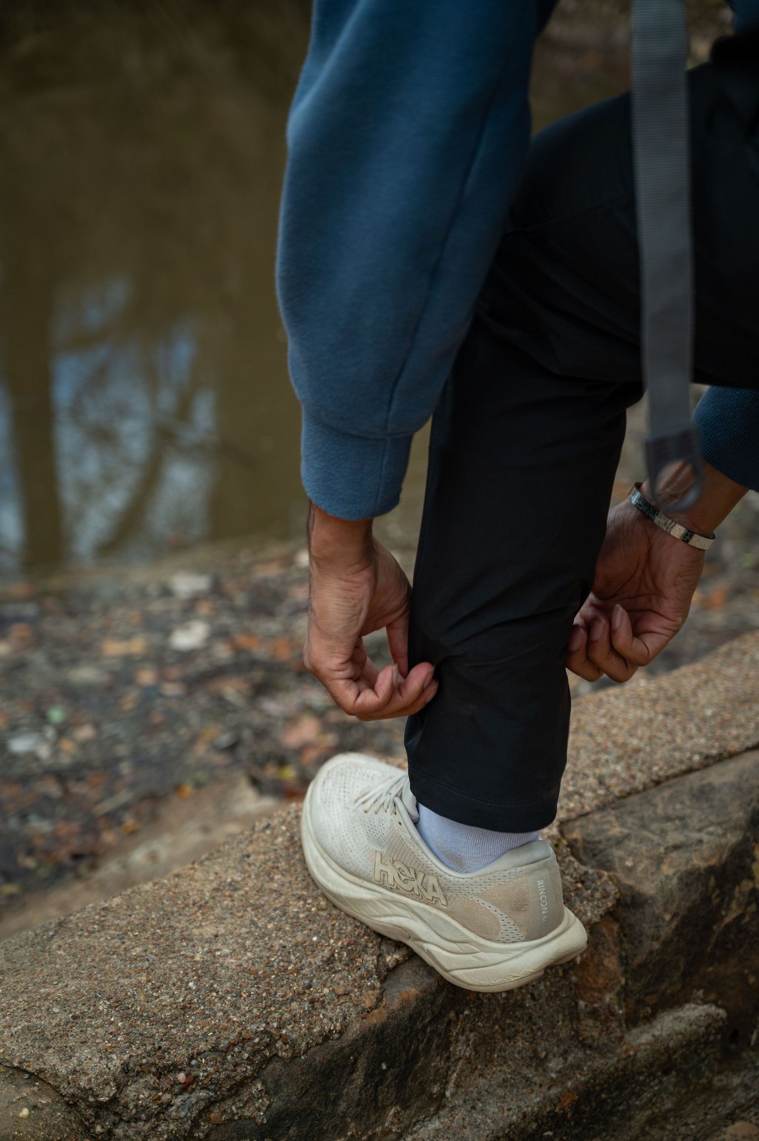 Close-up view of white sneakers and blue pants on a rocky surface near water.