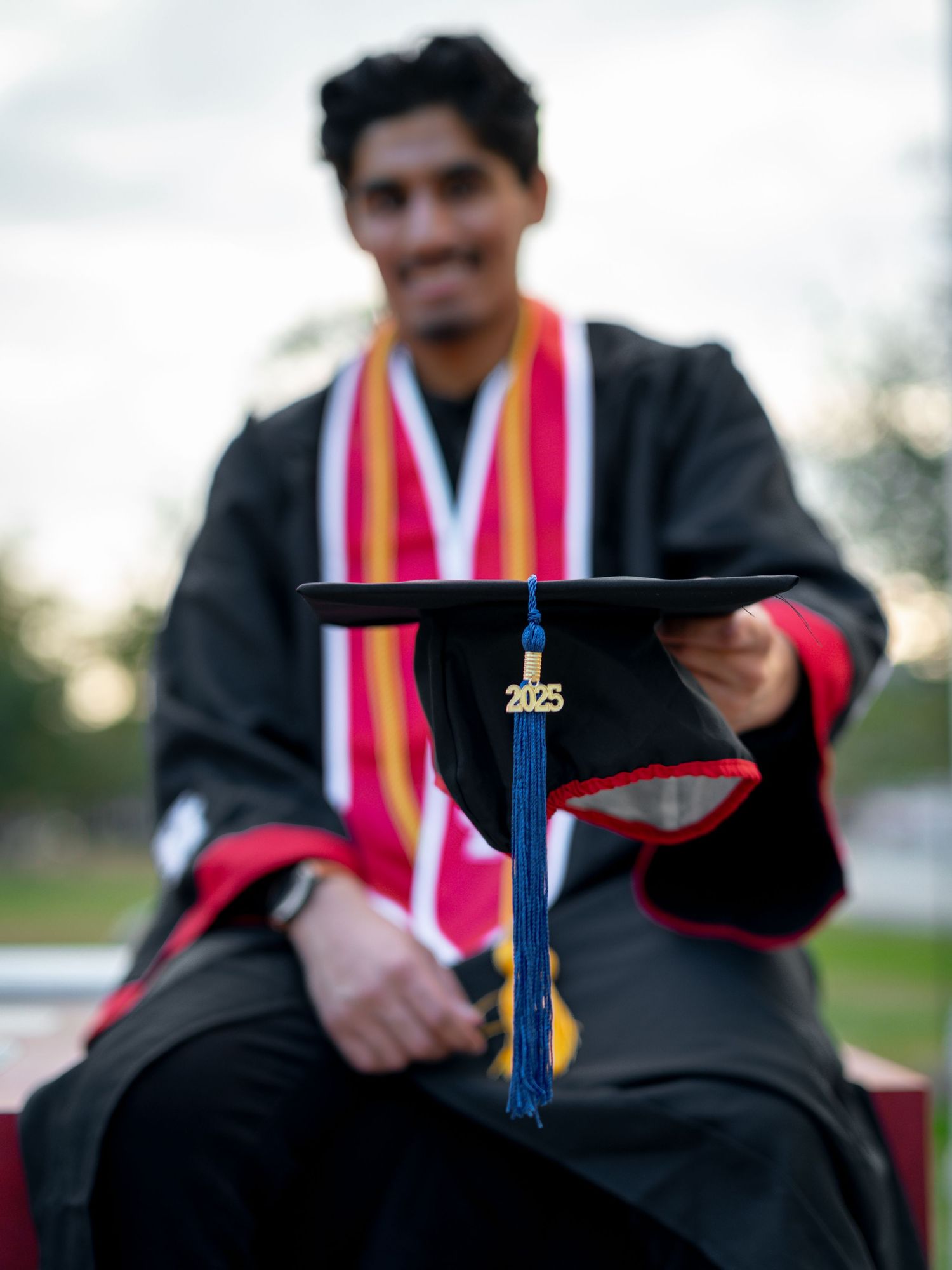 Graduate holding graduation cap against sunset sky during commencement.