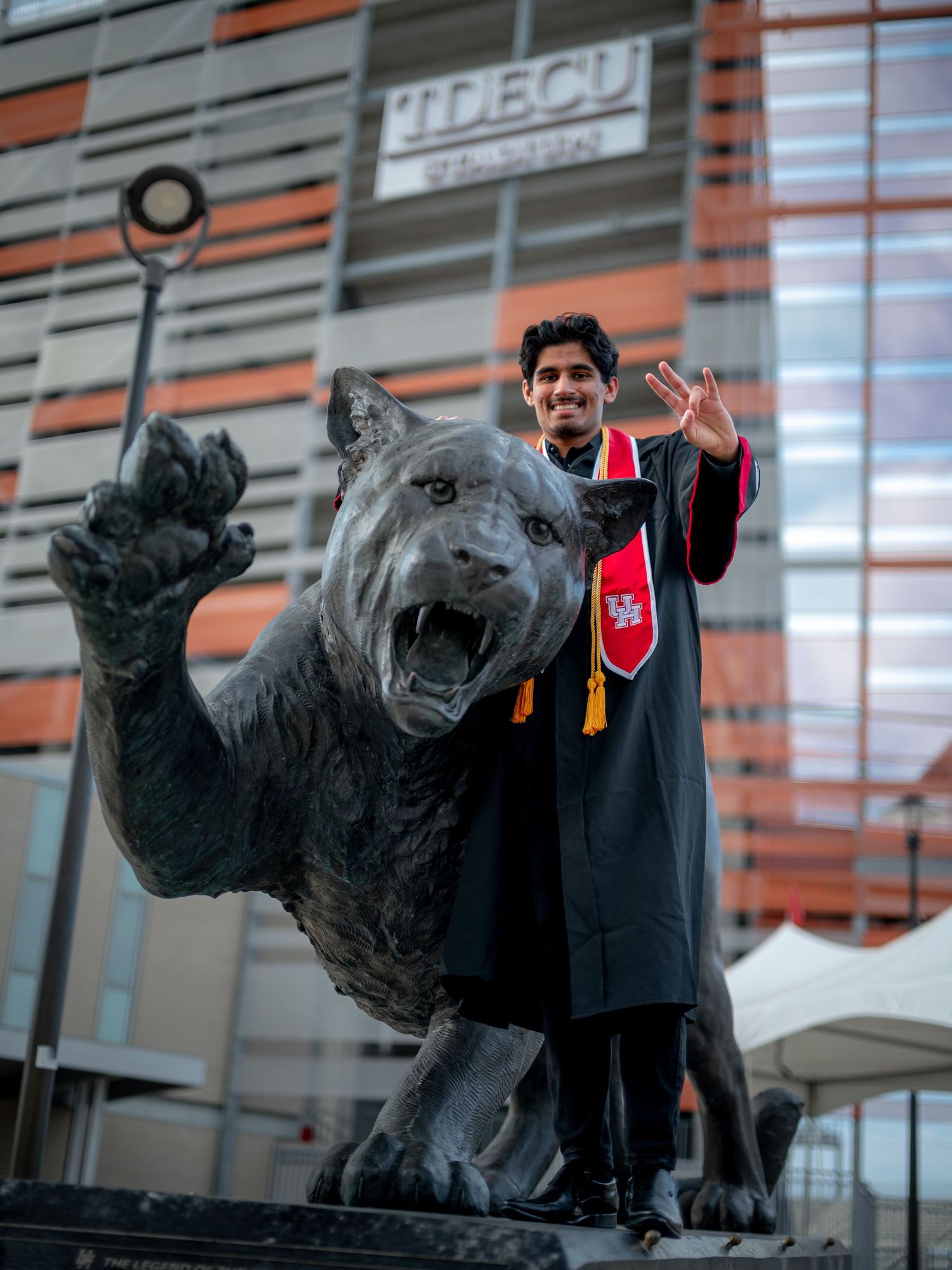 Graduate celebrating near large panther statue outside modern university building.