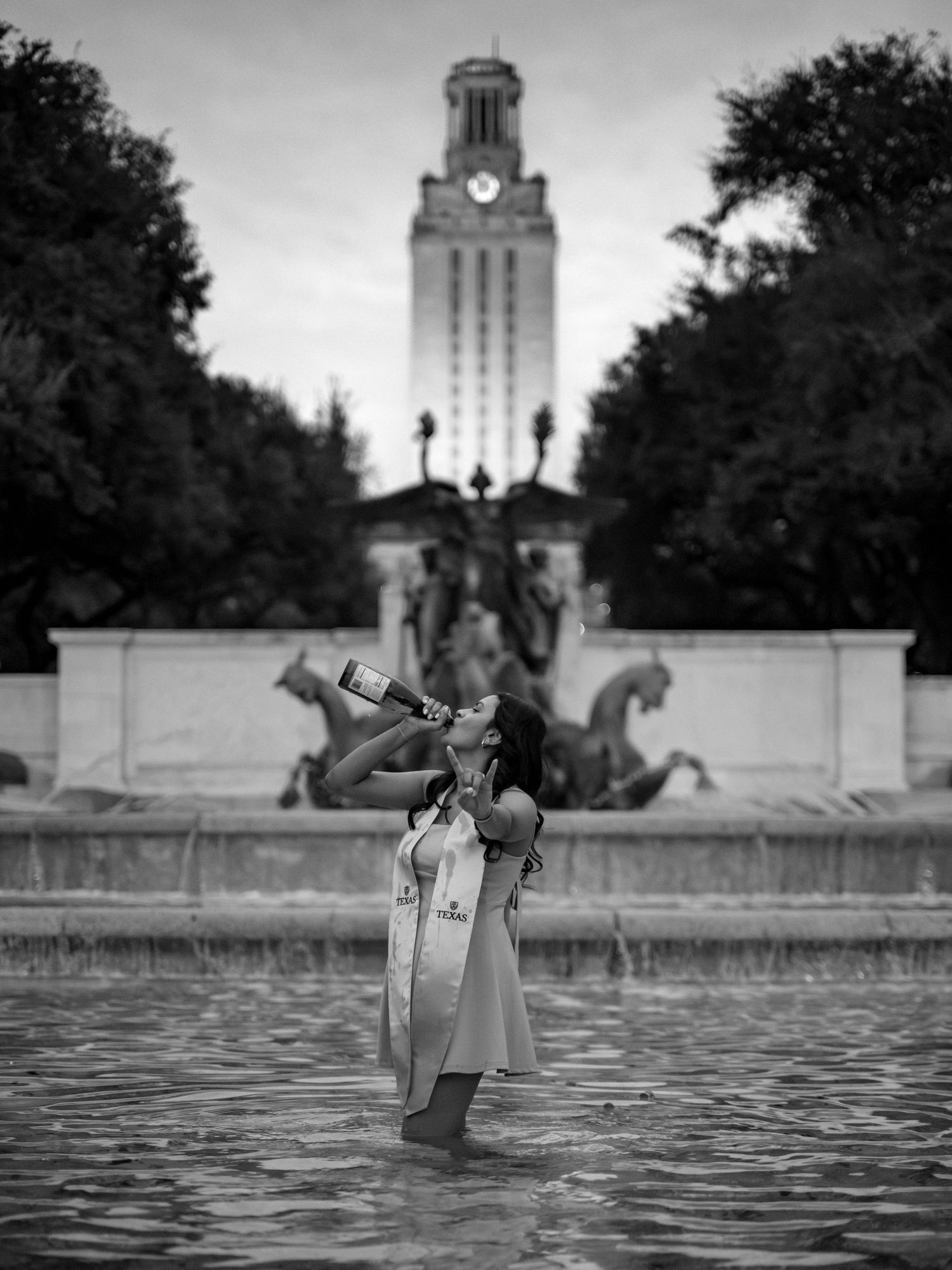 A person stands in the Littlefield Fountain at University of Texas with the iconic UT Tower illuminated in the background.