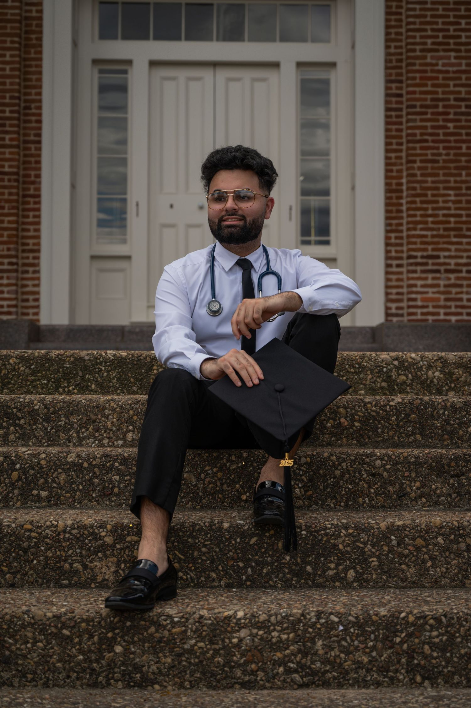 Medical graduate in white coat relaxes on concrete steps of academic building.