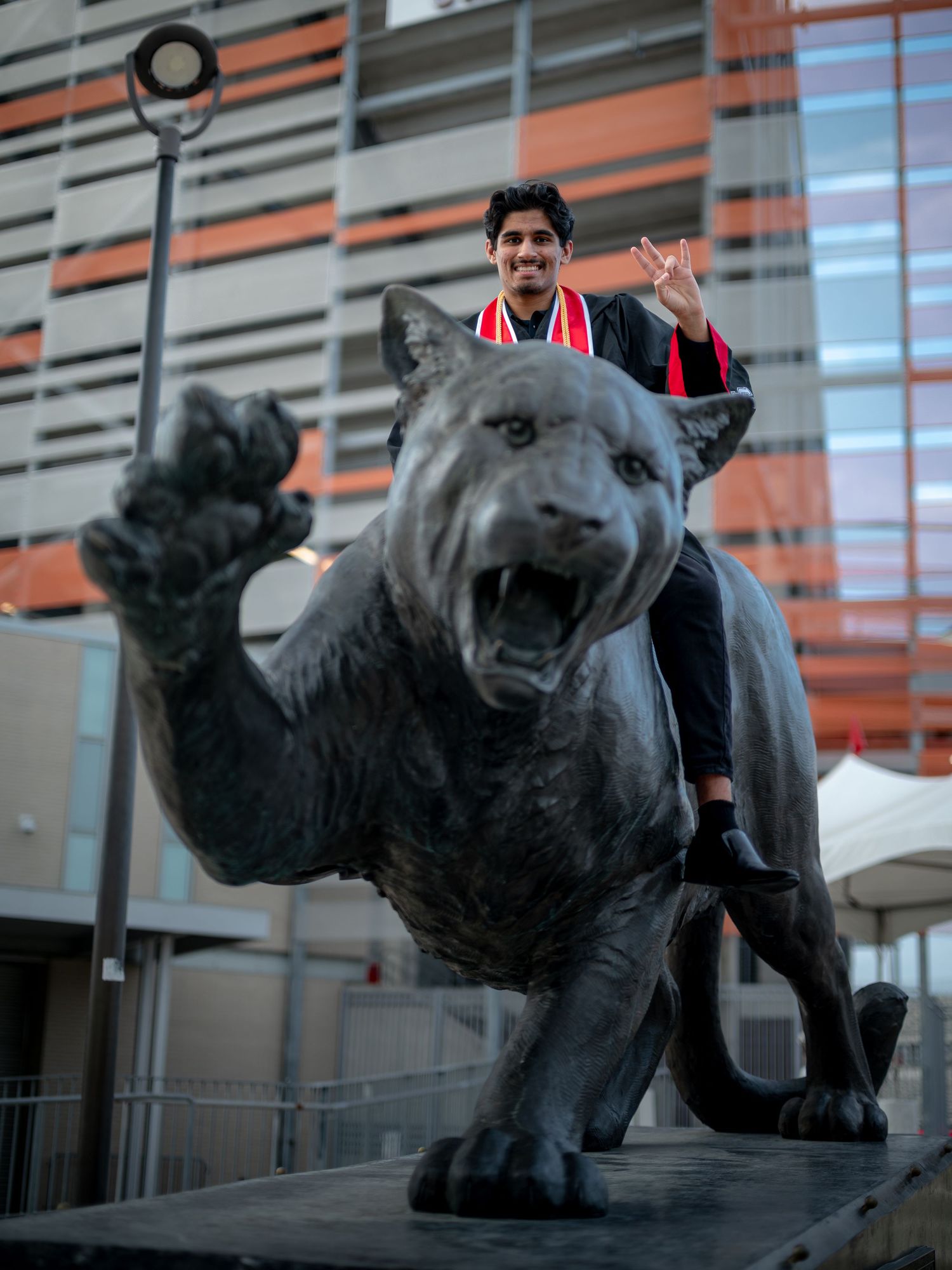 Graduate striking poses next to black panther mascot statues on campus.