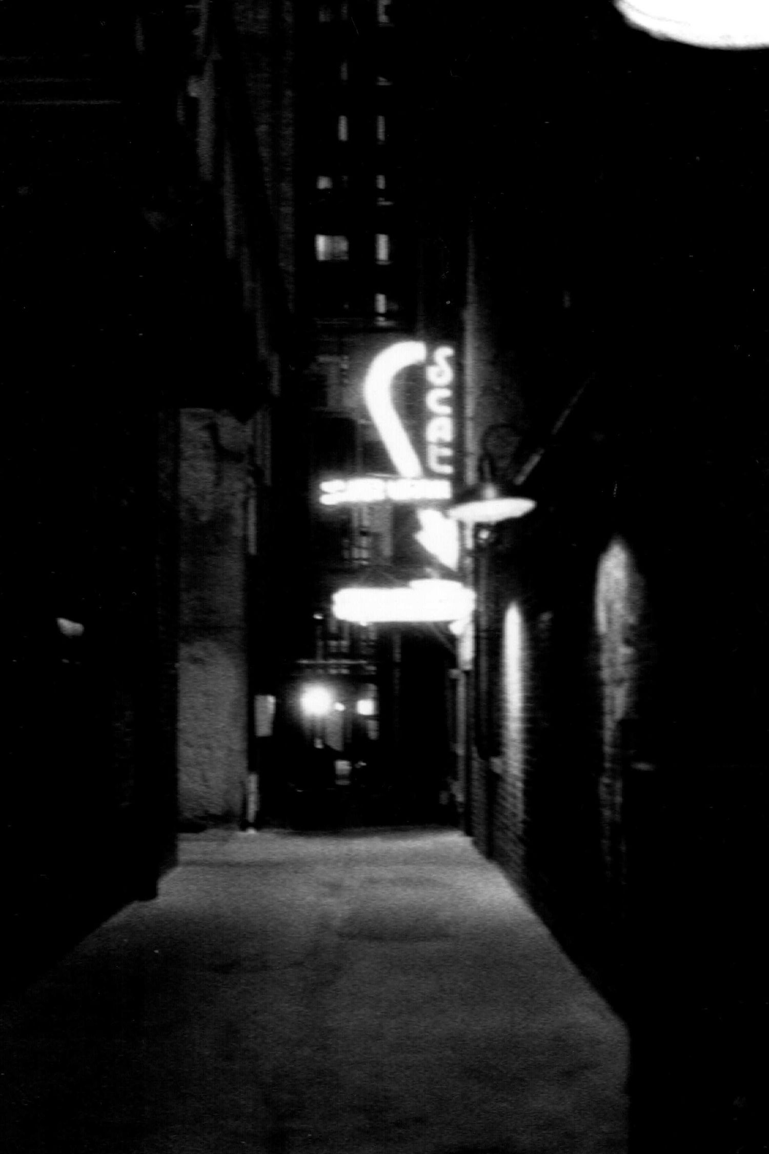 Illuminated neon signs glow in a dark urban alley at night.