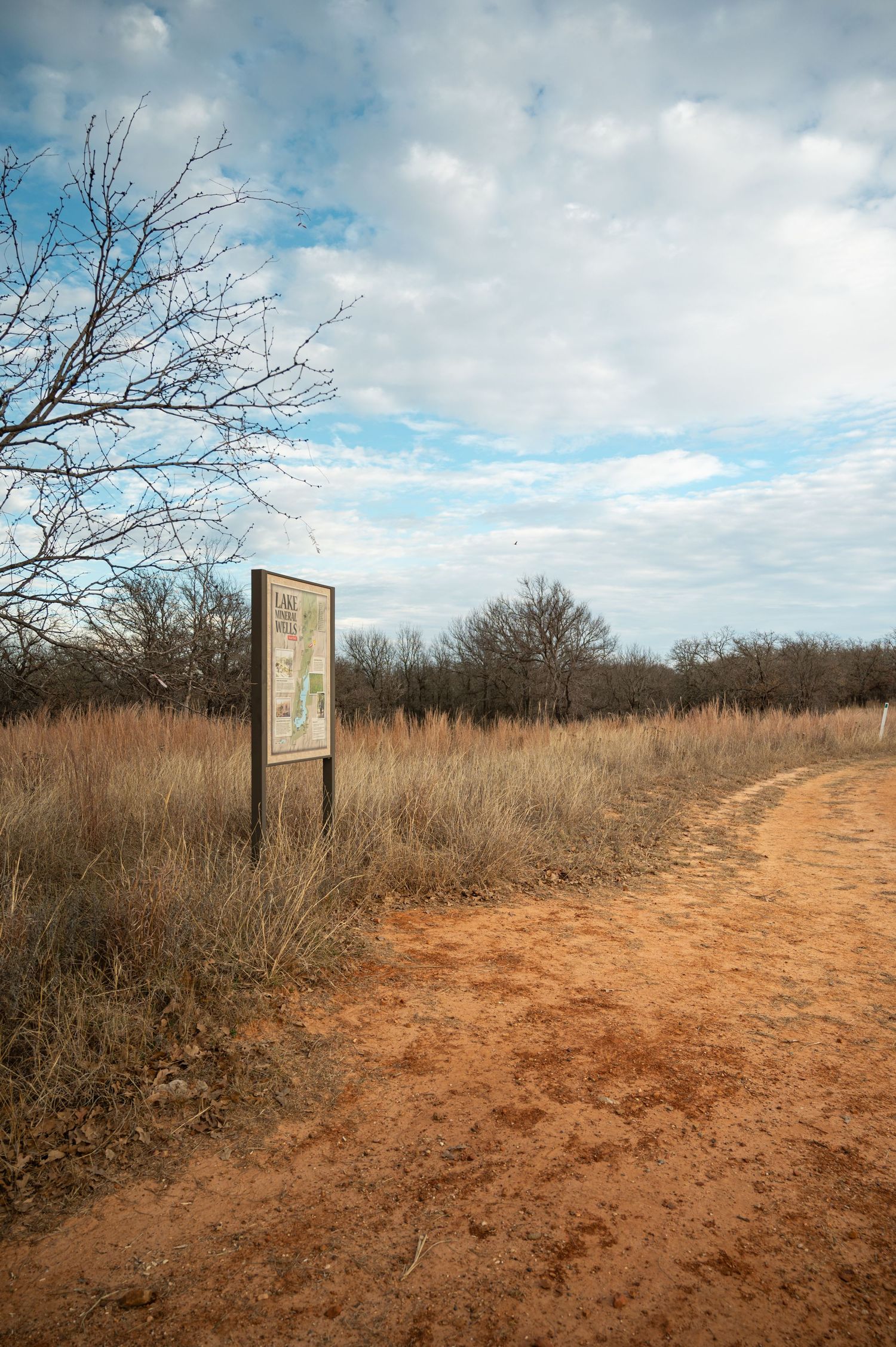 Dirt trail winding through dry brush with wooden trail markers and cloudy sky overhead.