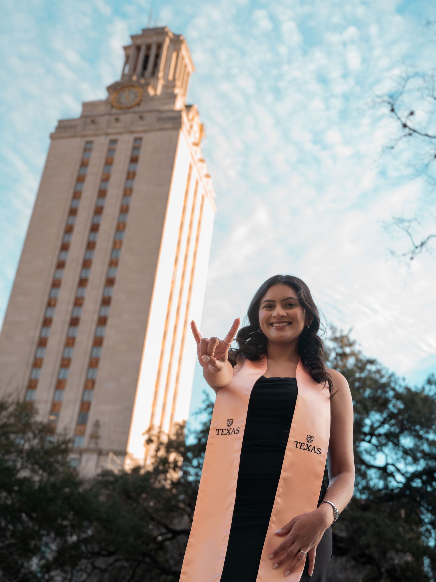 A graduate stands in front of the iconic University of Texas Tower in Austin on a bright sunny day.
