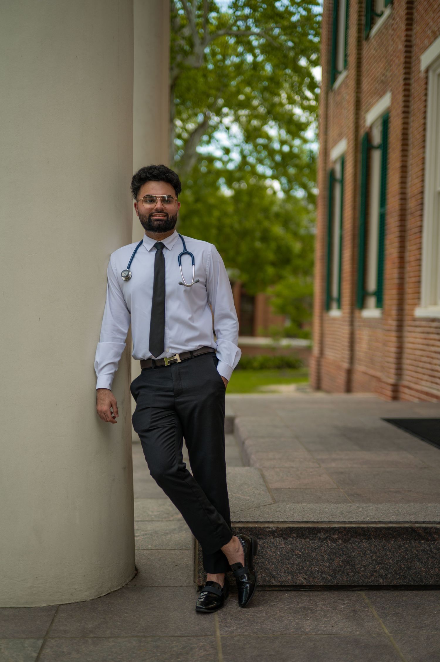 Graduate in professional attire poses along columned walkway of academic building.