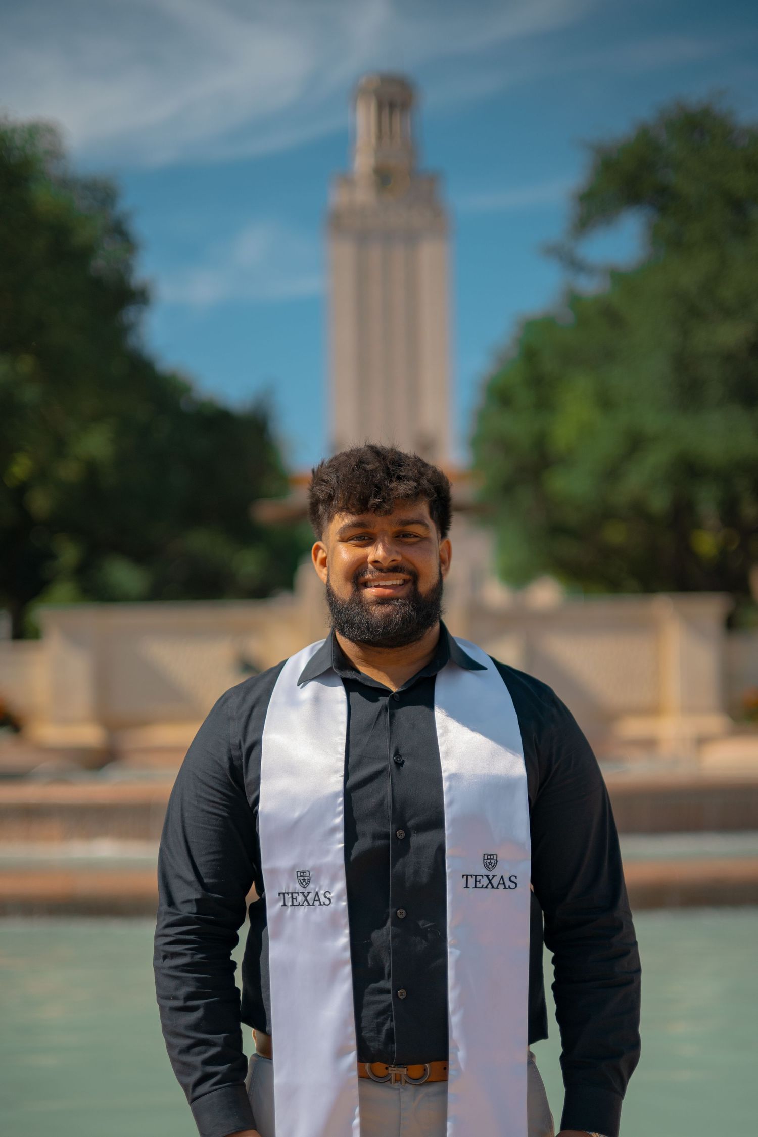 Graduate wearing graduation stole poses in front of iconic UT Tower and fountain.