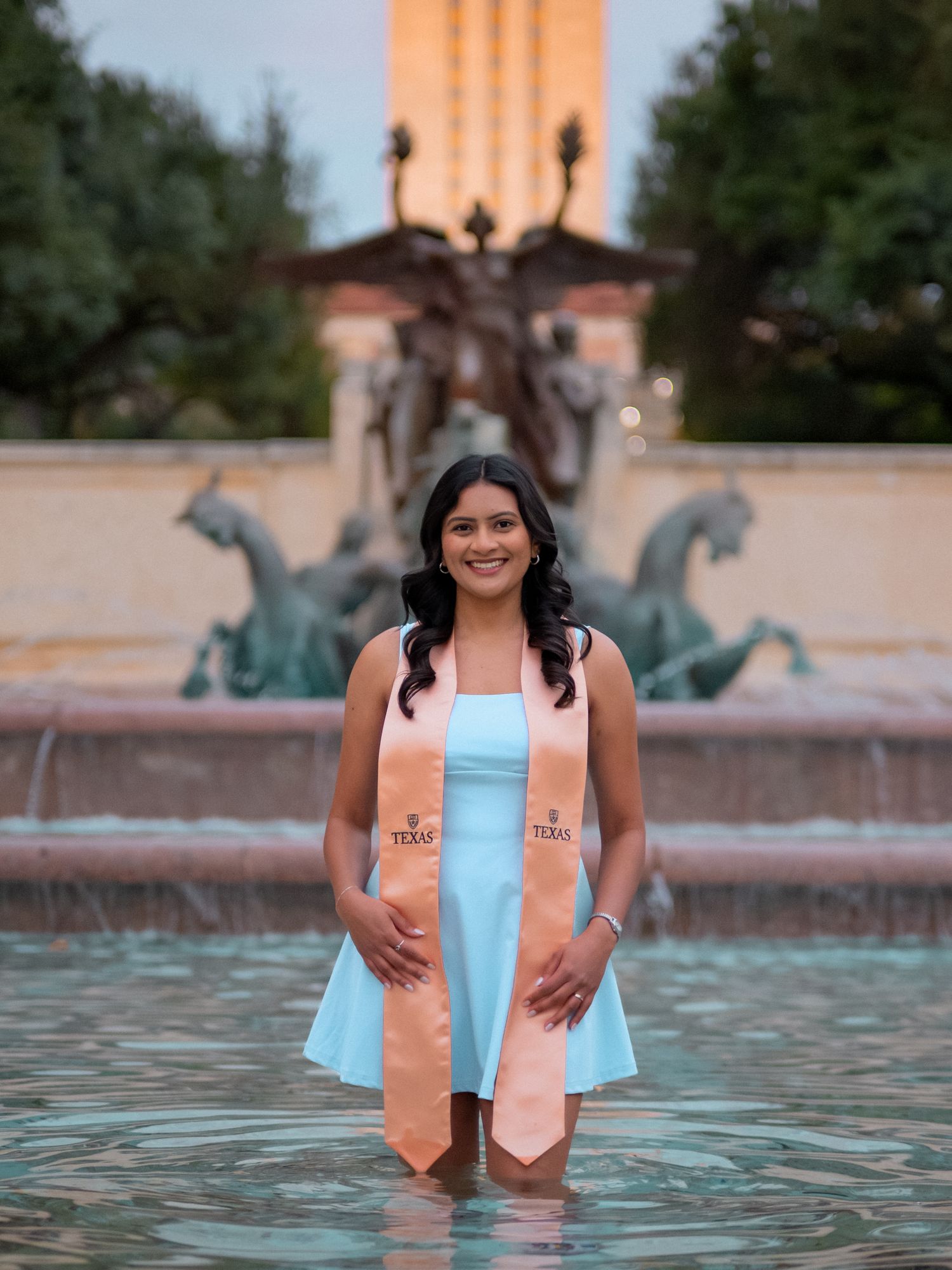 A series of graduation photos taken at a fountain showing someone in peach and blue graduation stoles posing at sunset.