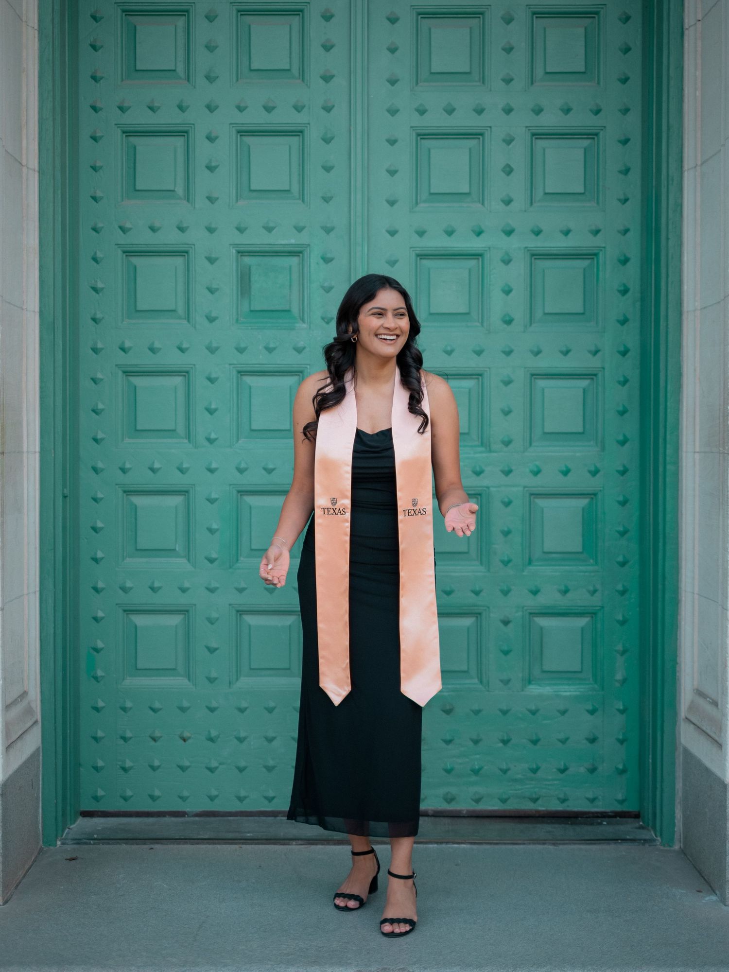 A graduation photoshoot series in front of turquoise doors showing poses in a black dress and pink stole.