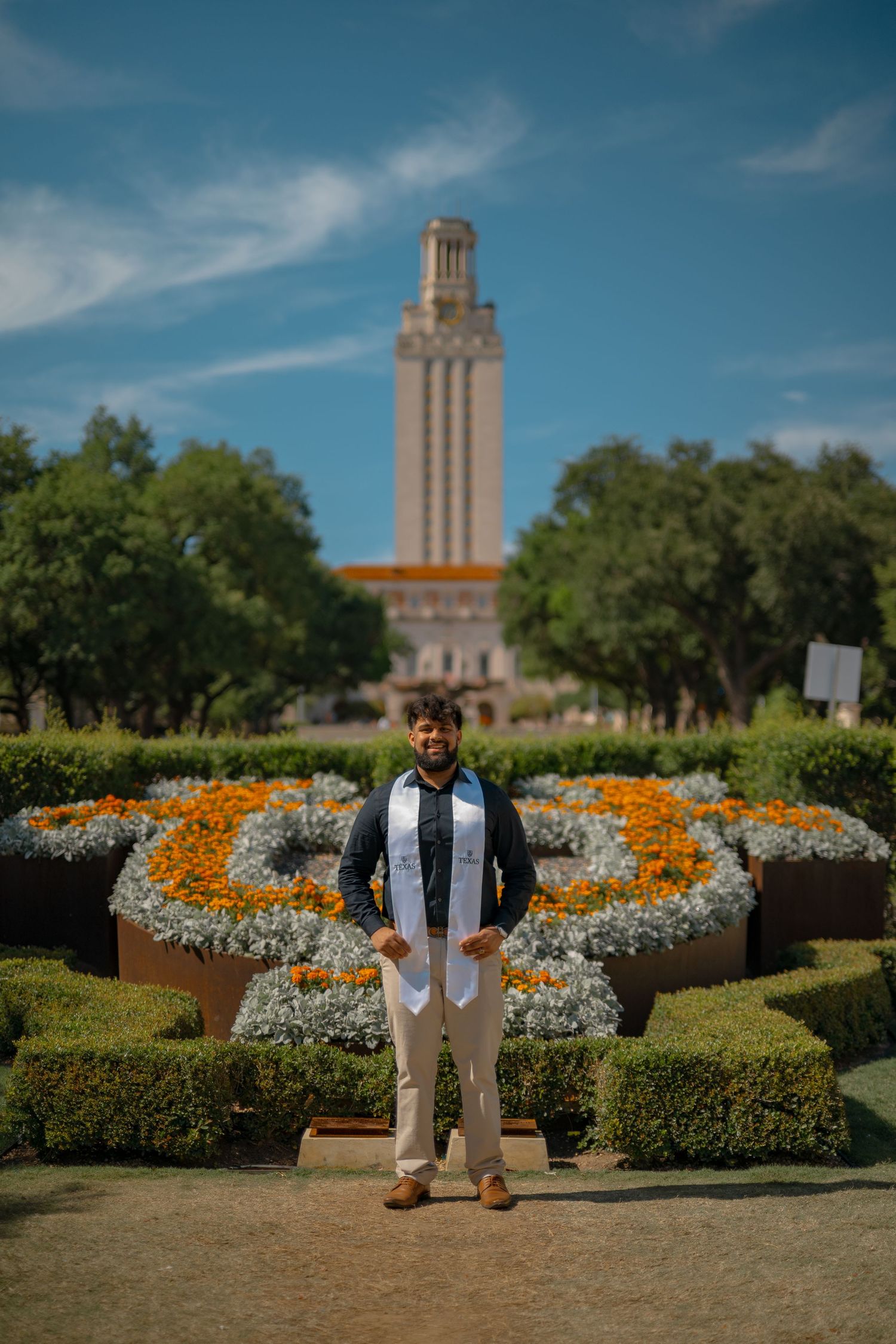 Graduation photos taken in front of the iconic UT Austin Tower with orange flowers in the foreground.
