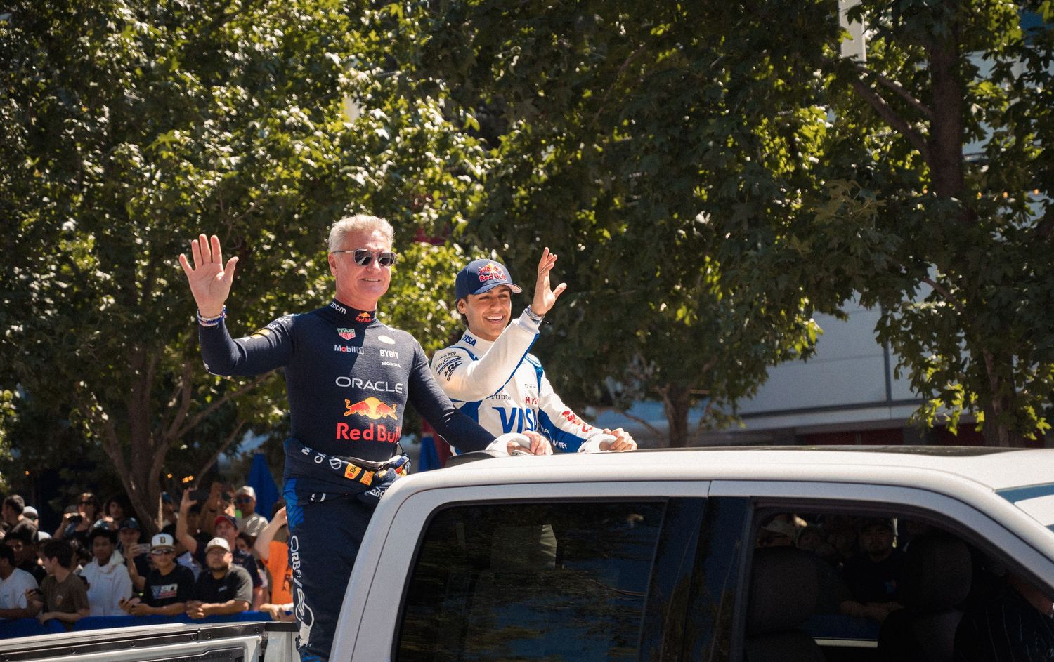 People waving from vehicles during outdoor celebration.