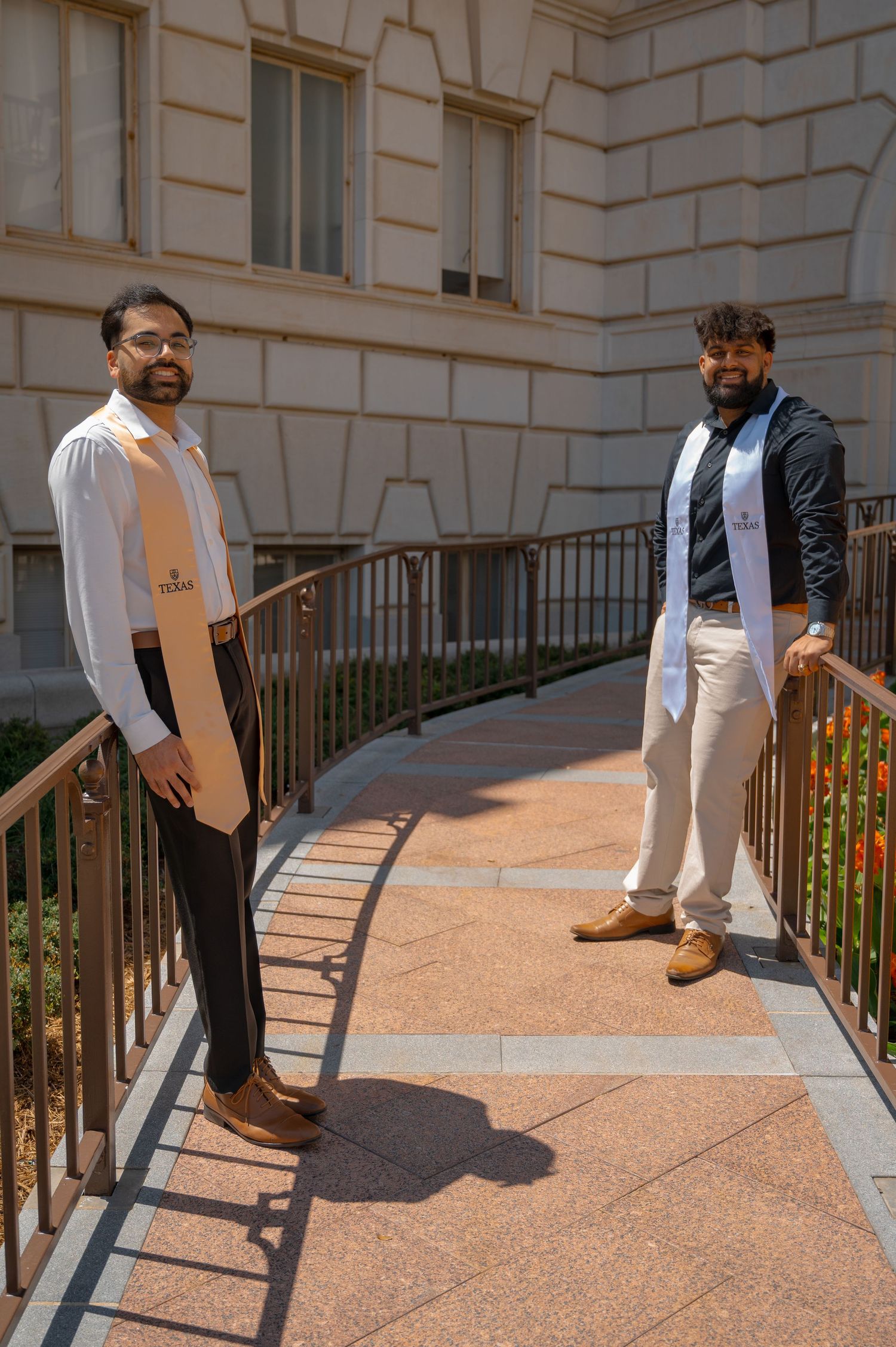 Graduate in formal attire poses on stone steps with decorative railing.
