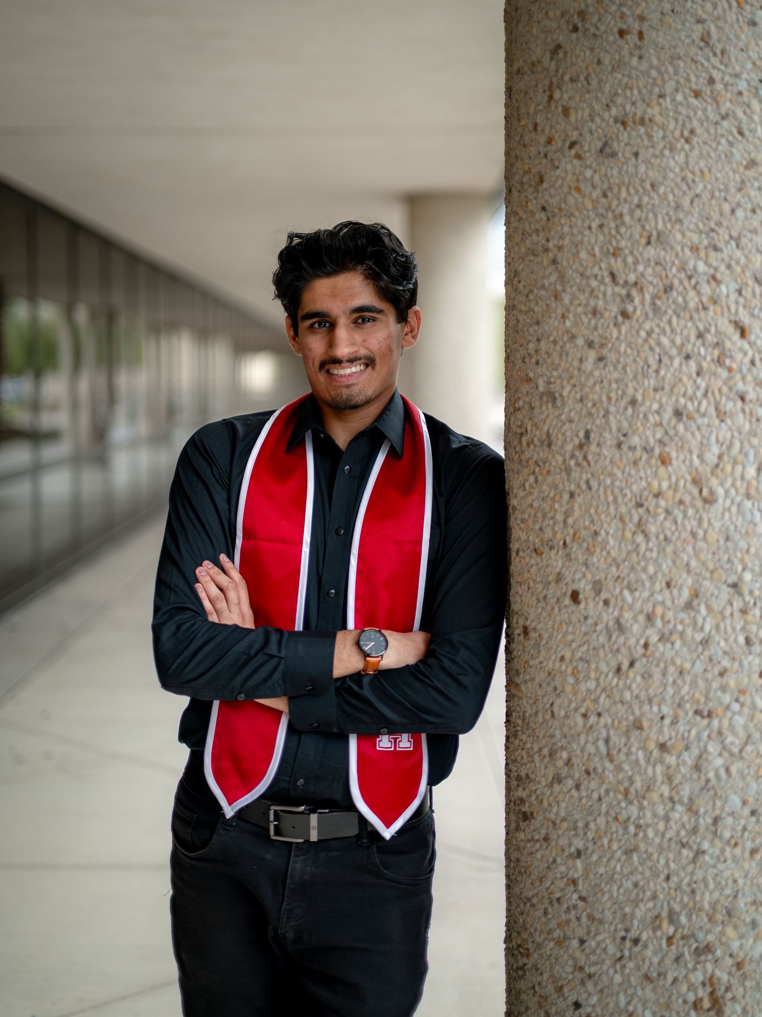 Graduate in academic regalia smiling and posing confidently between white columns.