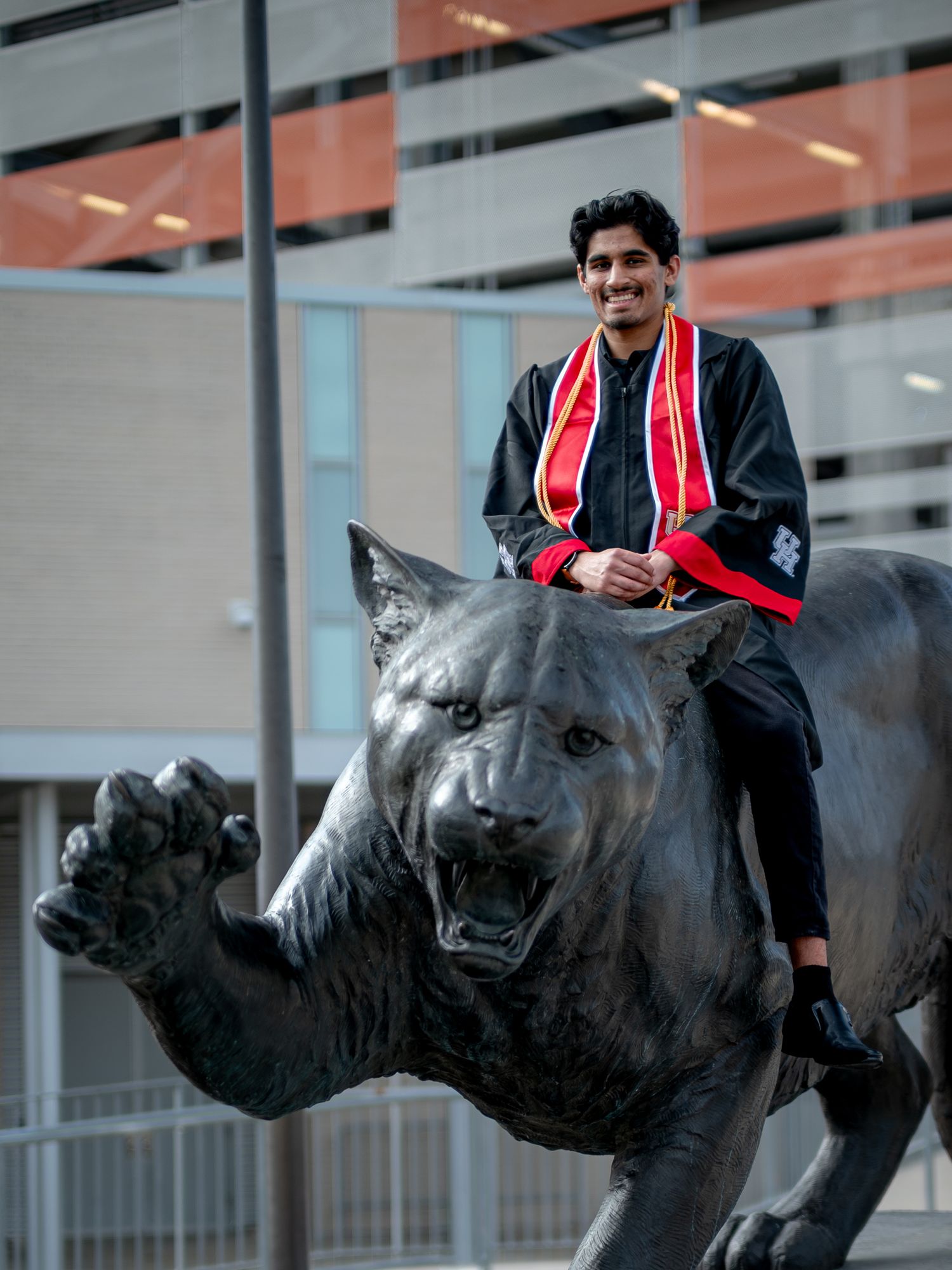 Graduate in academic regalia posing with row of panther statues at university.