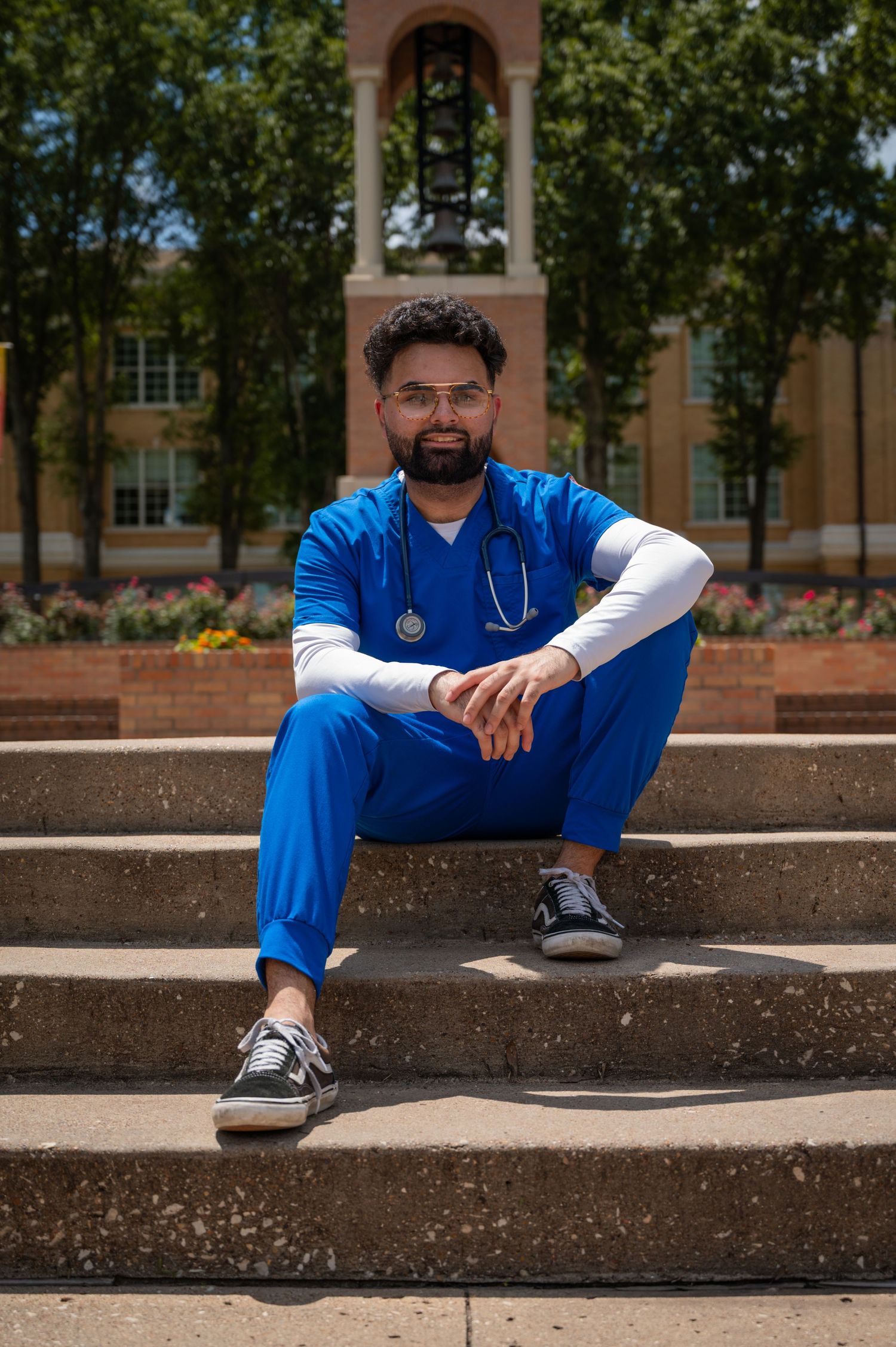 Medical professional in blue scrubs sits on concrete steps with stethoscope around neck.