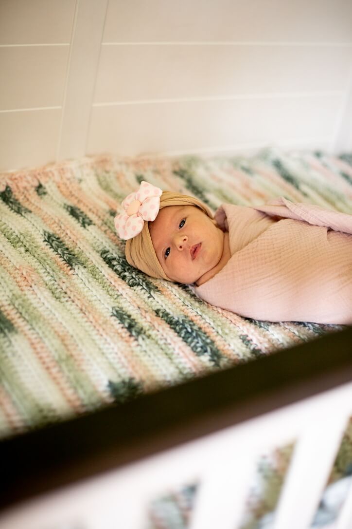 Indoor lifestyle family photography session with newborn in crib wearing a bow in Omaha, Nebraska