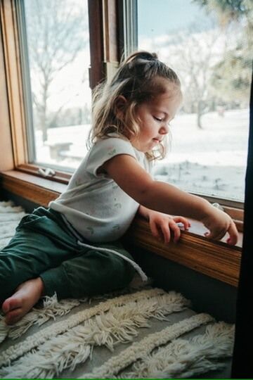 Indoor lifestyle family photography session with child looking out window in Omaha, Nebraska