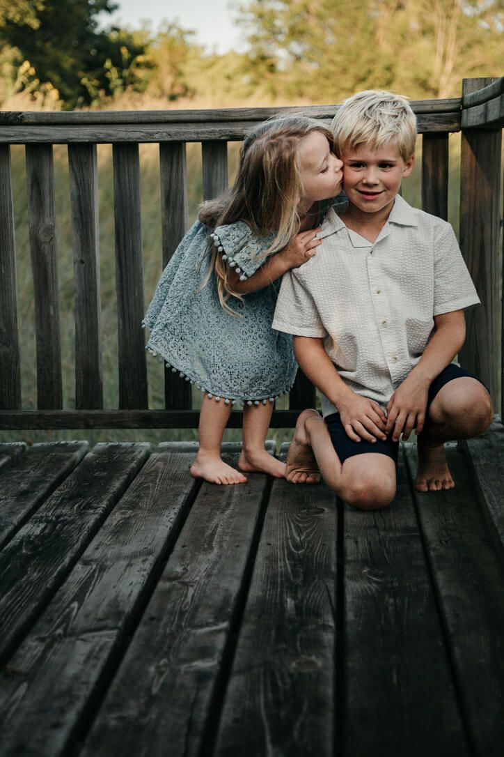 Outdoor lifestyle family photography session with sister kissing brother in Omaha, Nebraska