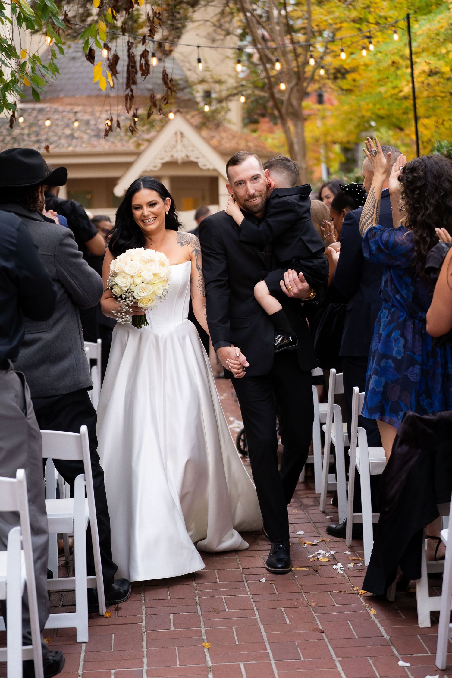 Wedding guests seated in white chairs during an outdoor autumn ceremony.