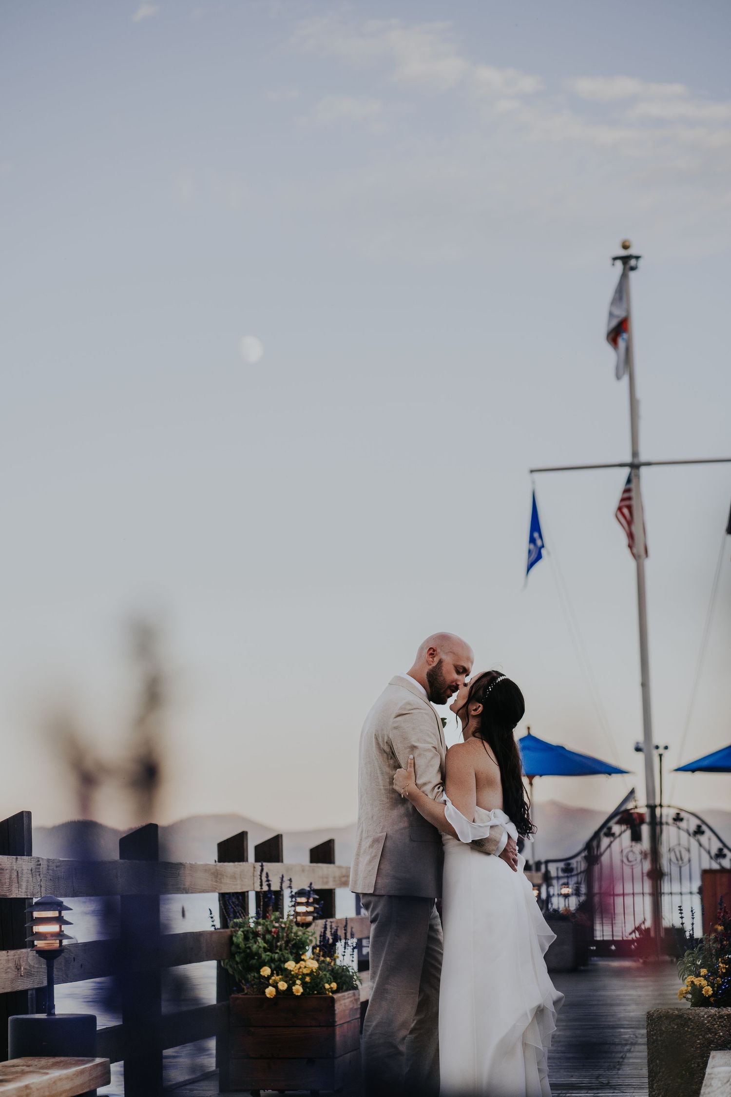 Wedding ceremony on a waterfront boardwalk with flags and blue sky.