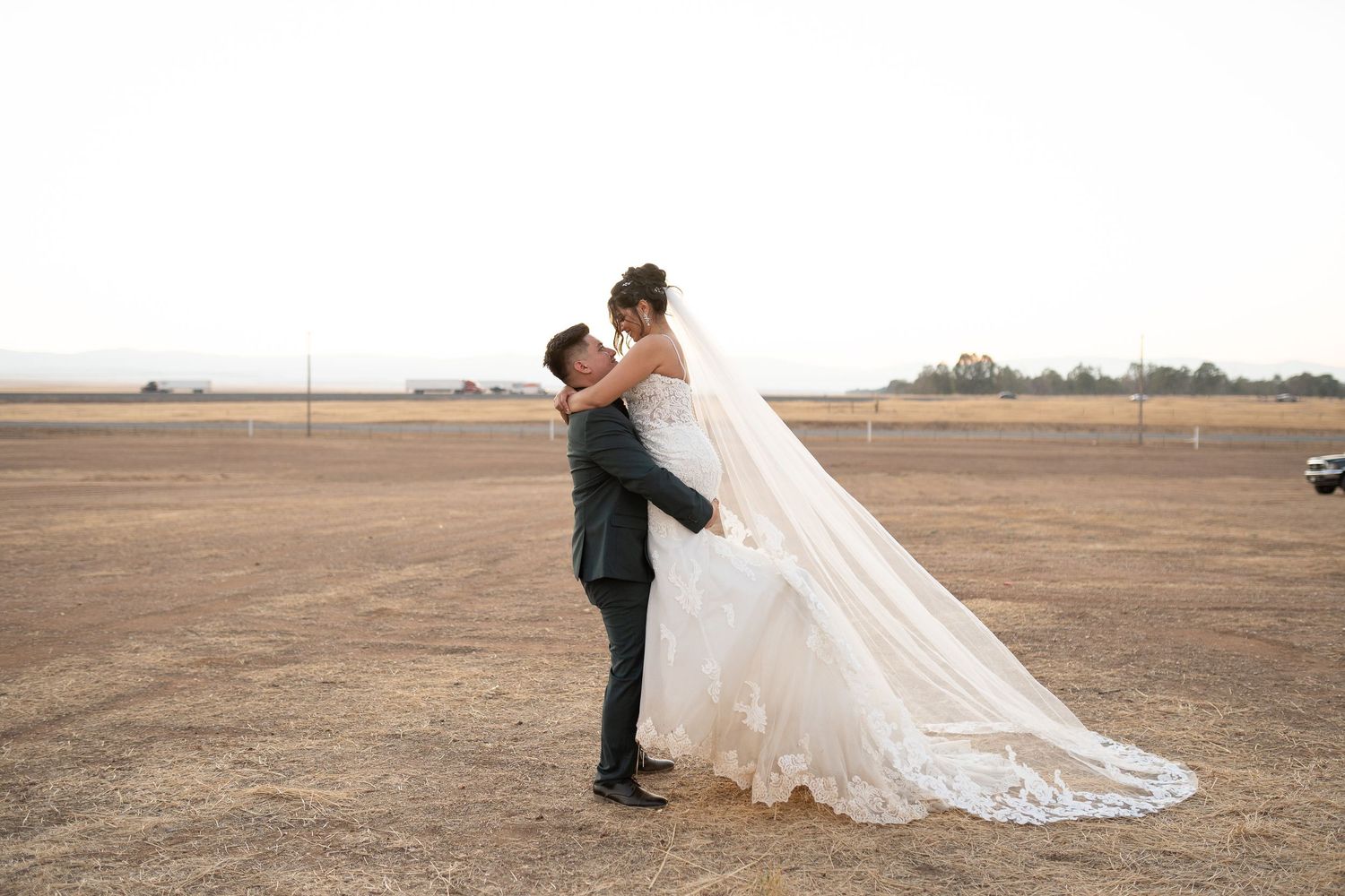 Wedding couple embracing in a vast open field with dramatic sky.