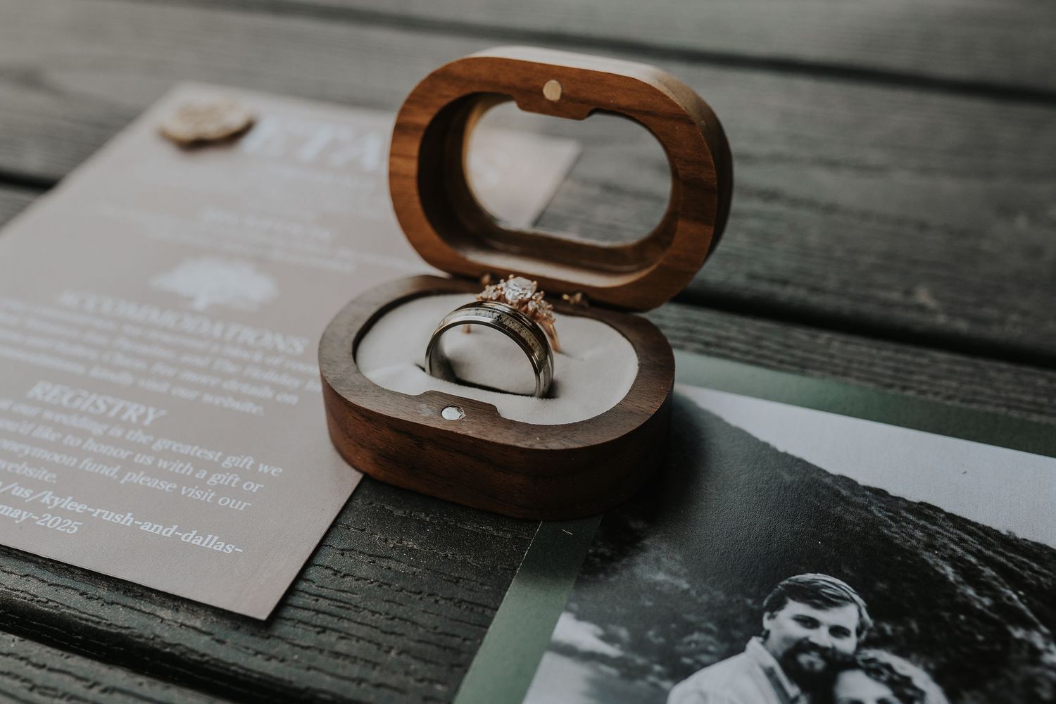 Wooden ring box and wedding stationery arranged on dark wood surface.