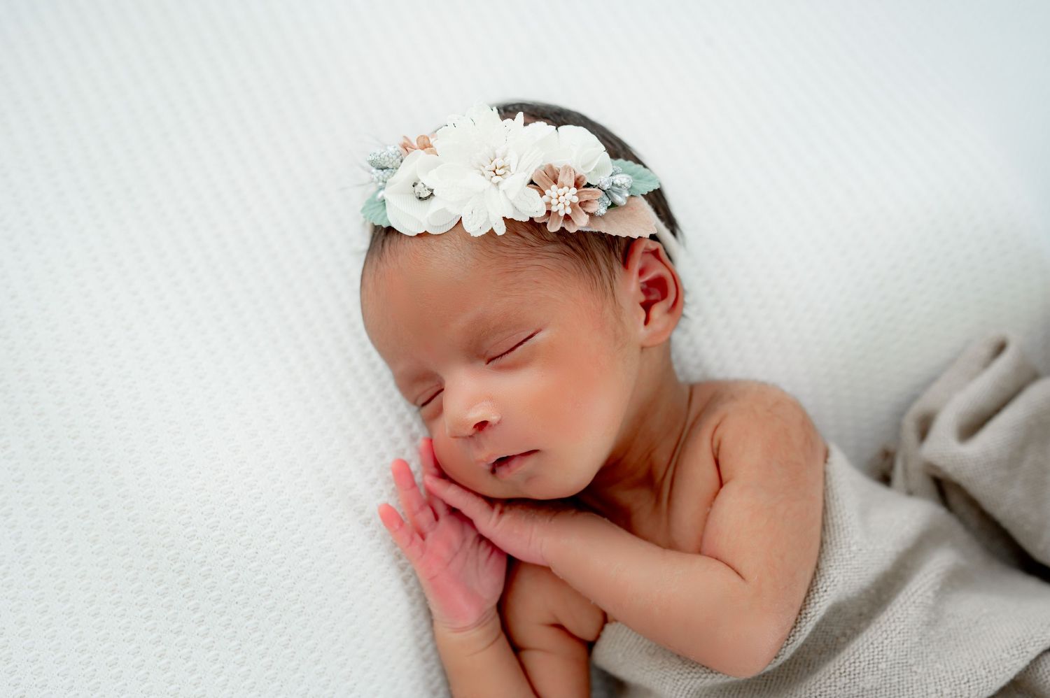 A newborn studio session in Fulshear, TX with a side lying sleeping baby girl wearing a flowered headband.